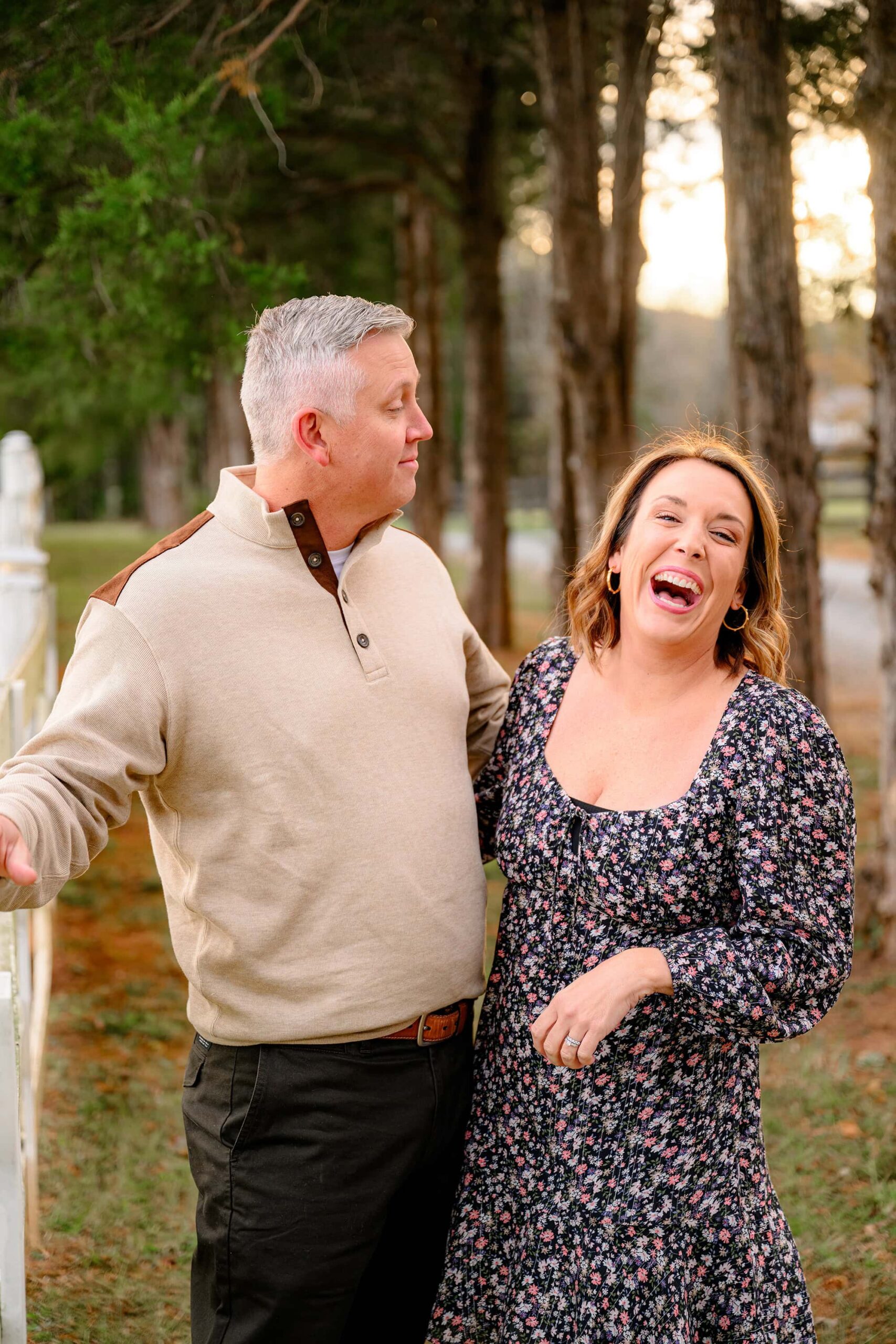 husband looks at his wife who is laughing during their family photography session at a waxhaw park