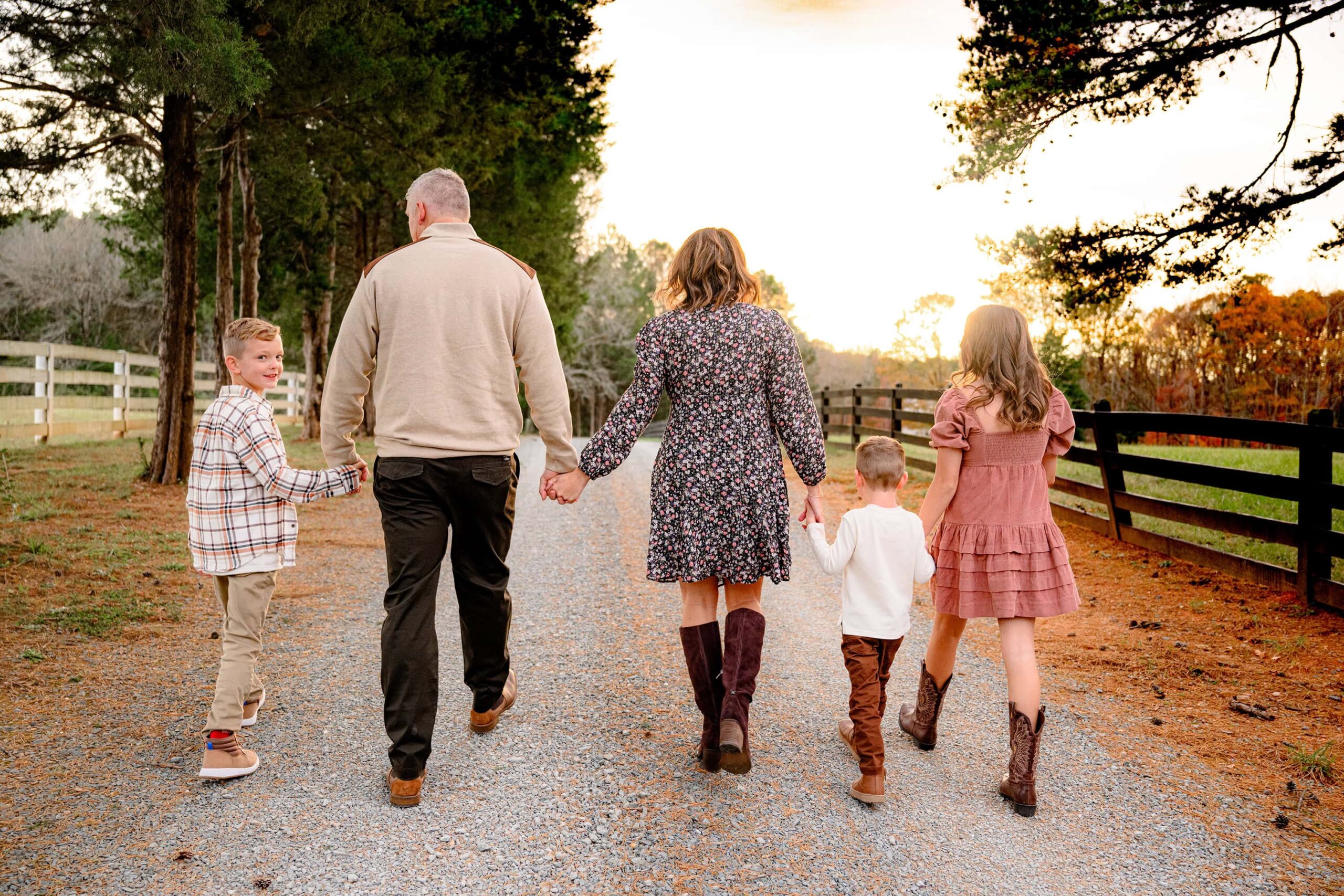 family walking hand in hand in a waxhaw park while middle son looks back smiling 