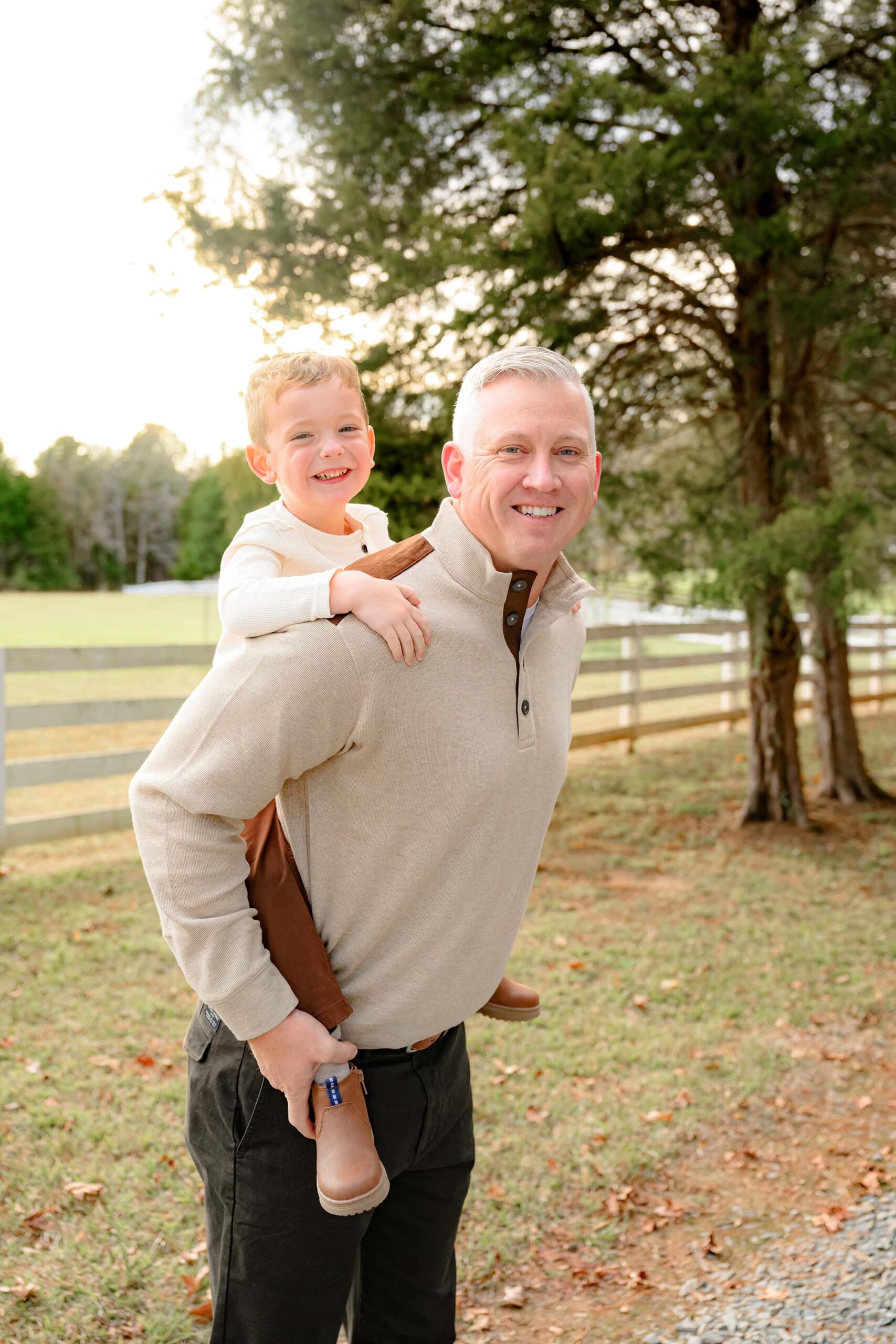 father holds his son on his back laughing together during family photos