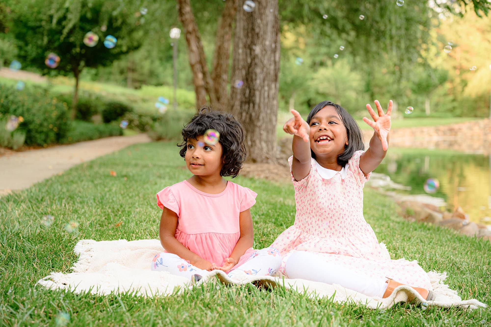 two sister sit on a summer day in a charlotte park playing with bubbles all around them!
