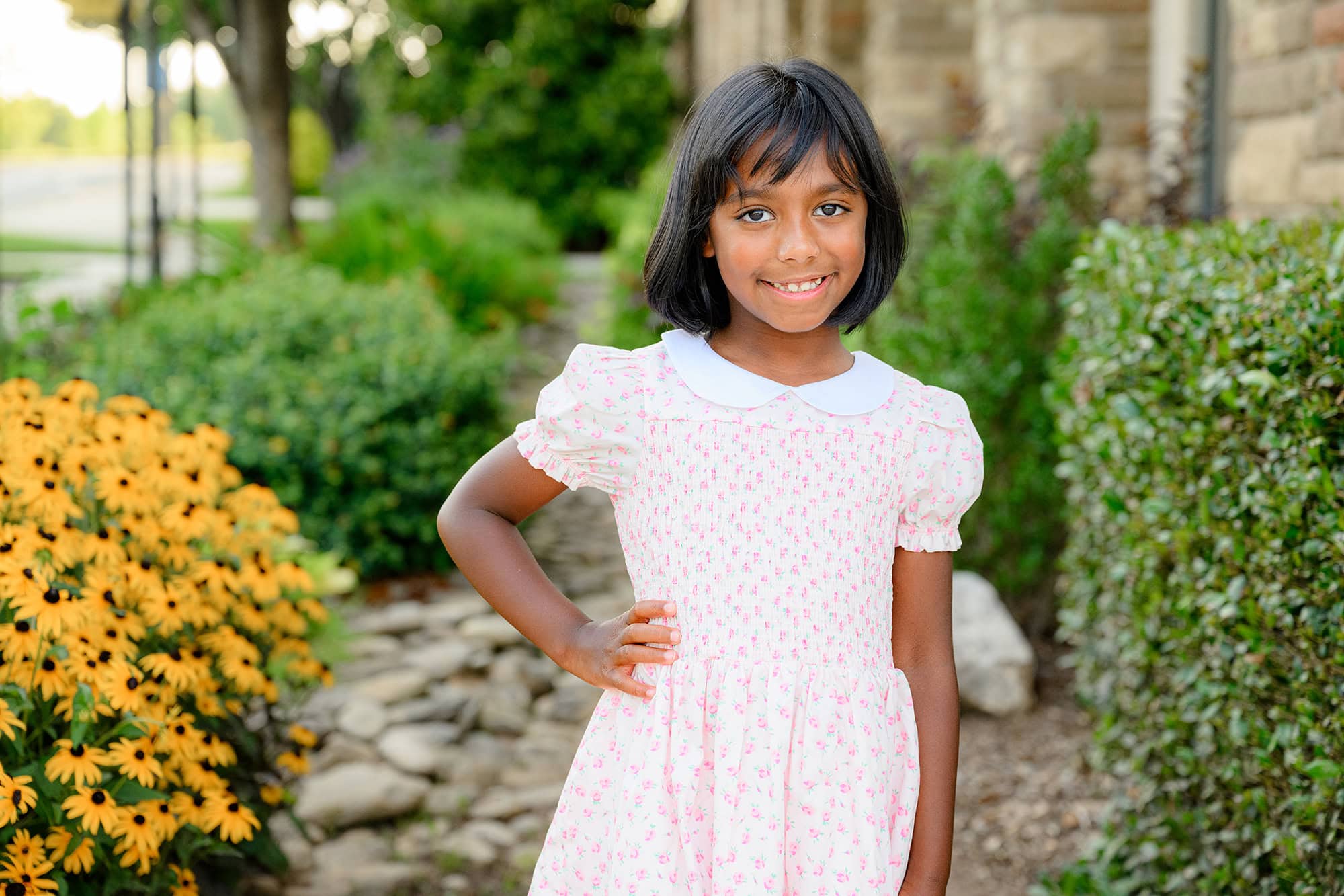 oldest daugter of a charlotte family stands in a flower garden on a hot summer day with her family wearing a floral dress