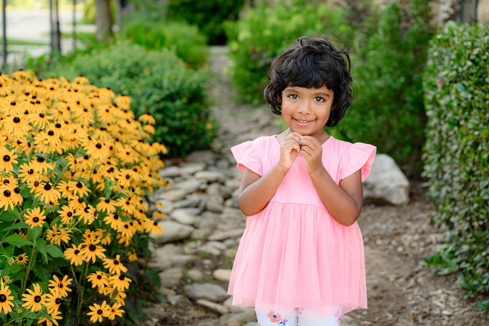 youngest daughter wears a pink top and floral pants as she stands in a charlotte flower garden on a summer da