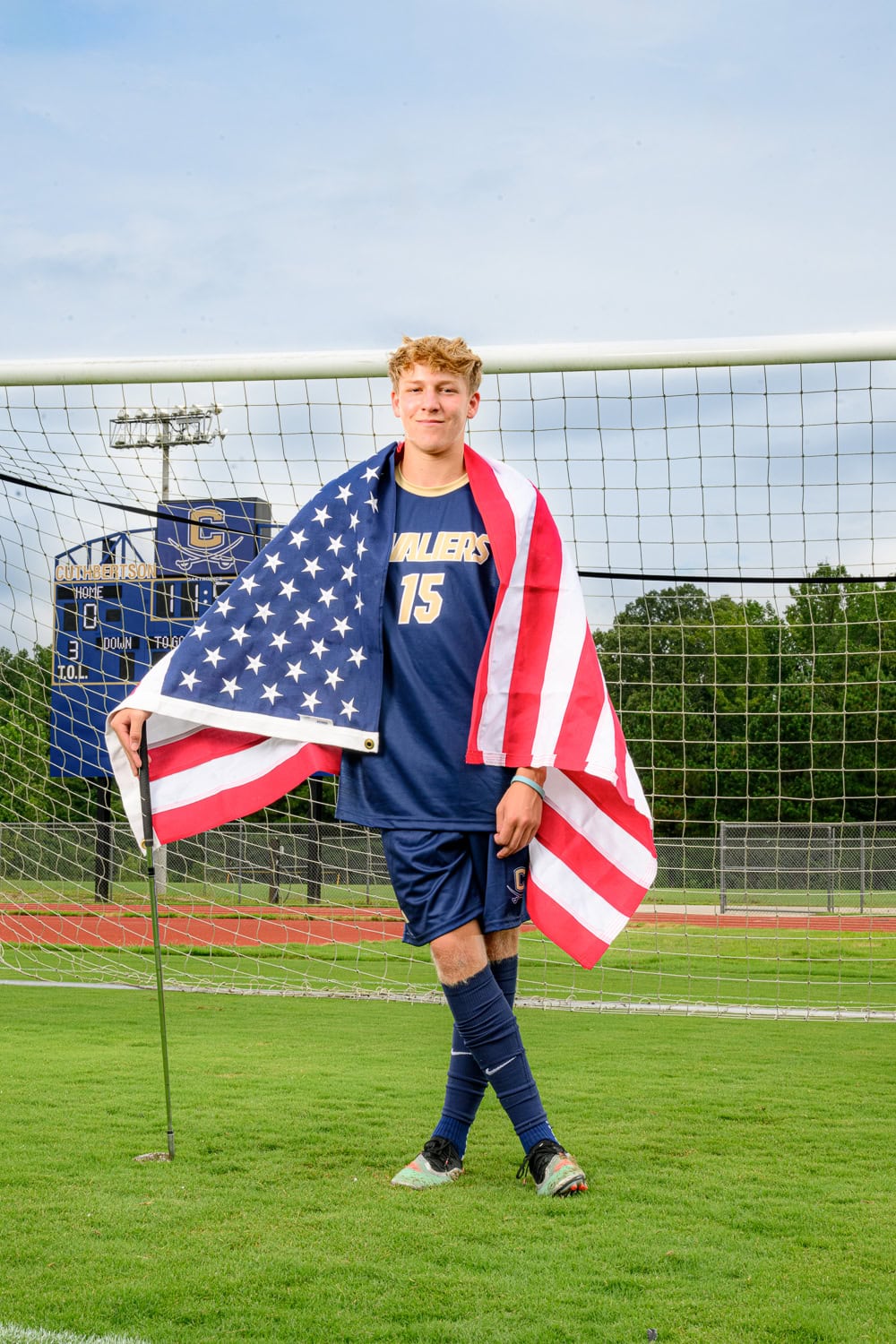 Senior photo of CHS mens soccer player with american flag draped around his shoulders and holding a golf club