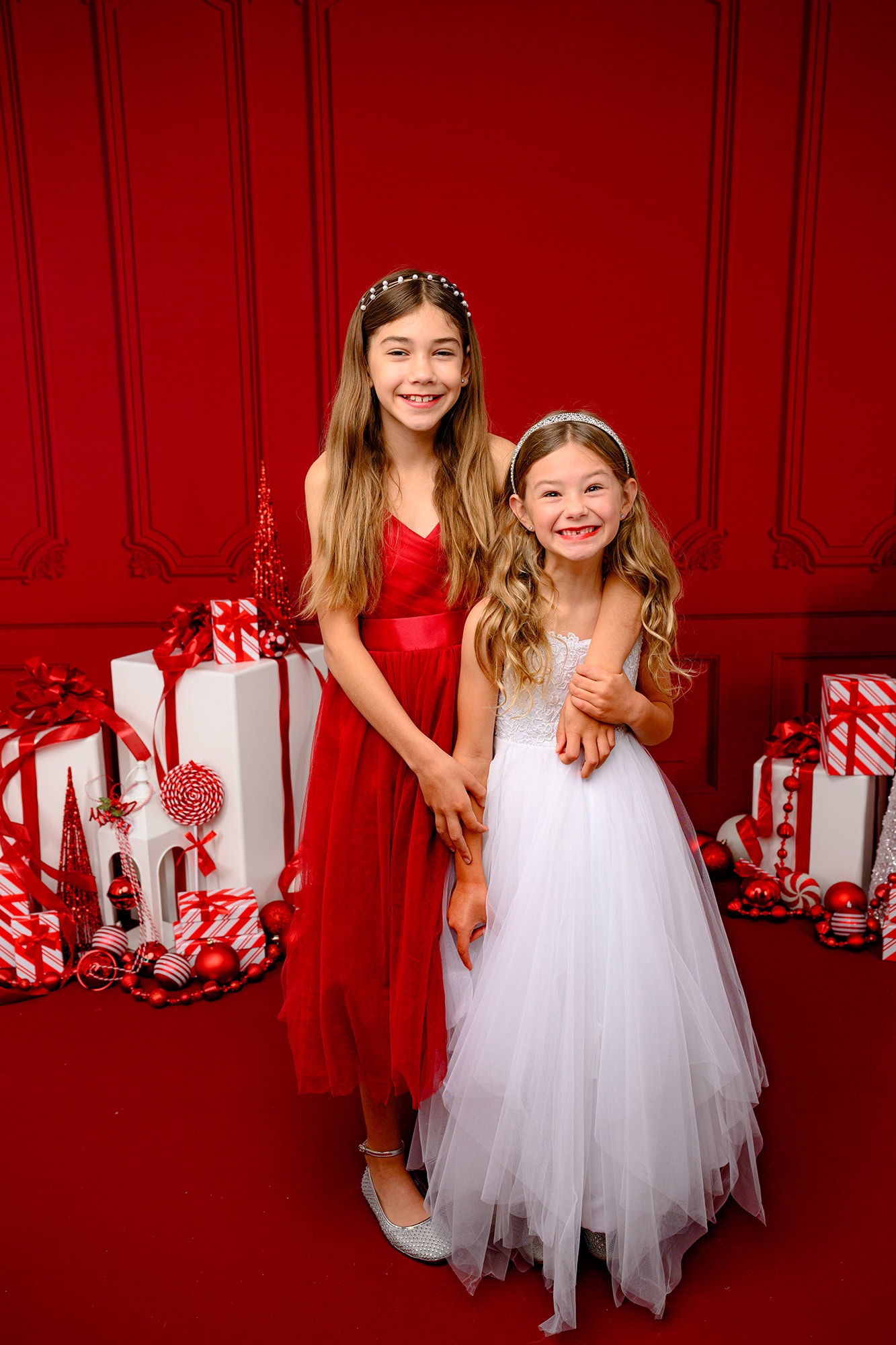 red studio set up with two sisters standing together surrounded by present props