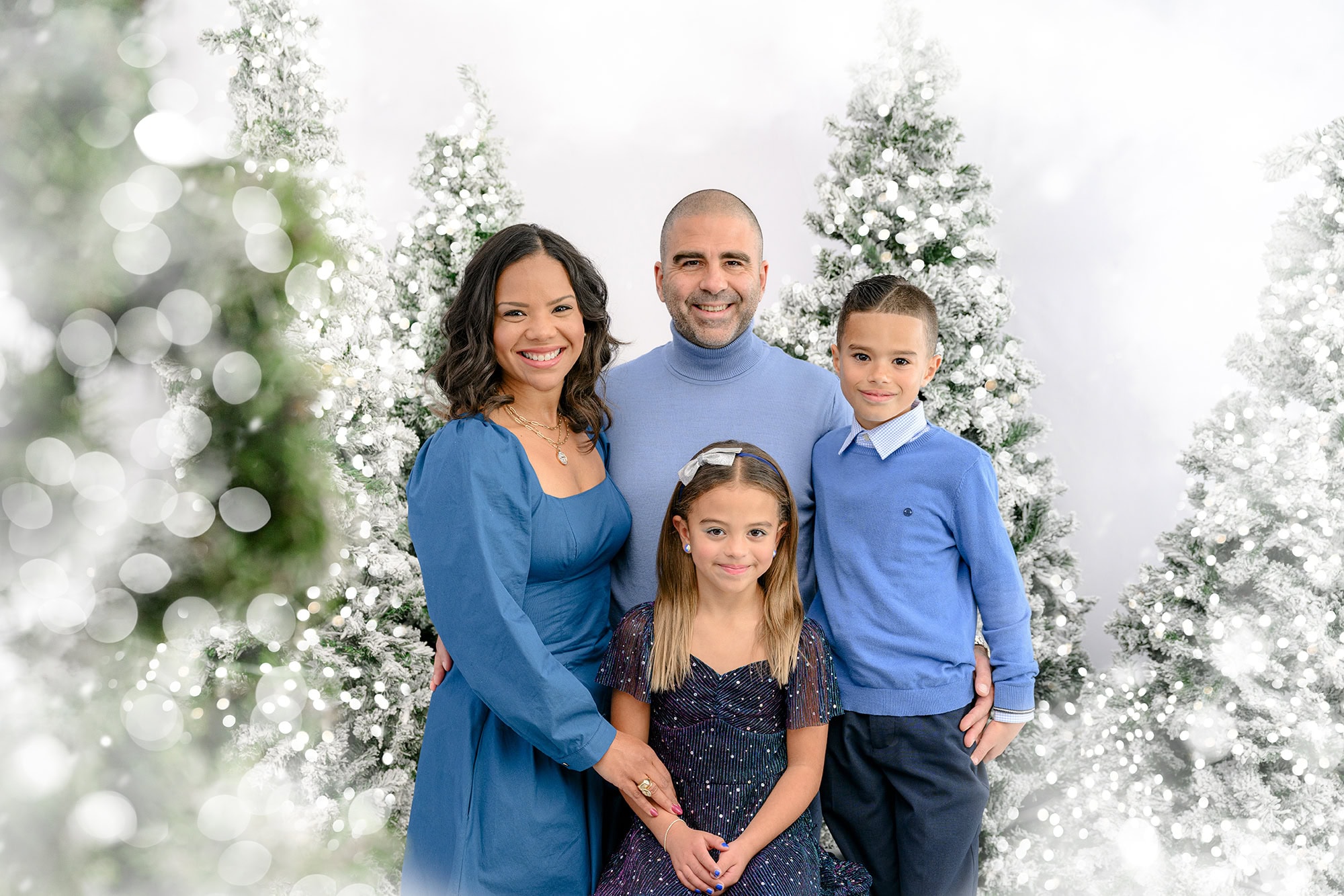 Family of four dressed in blue in a holiday winter white studio session set up