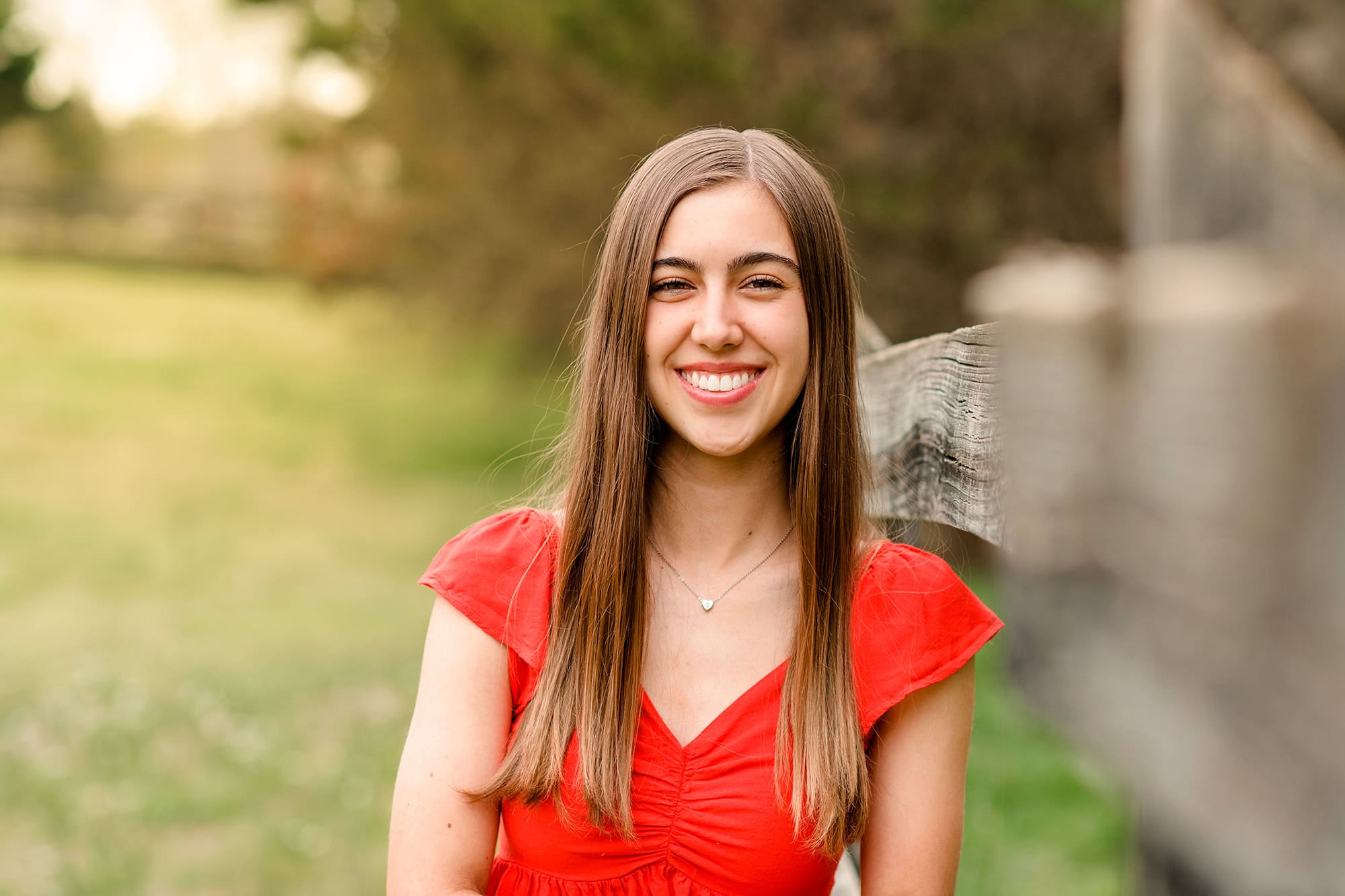 graduate leans against fenceline wearing a red shirt