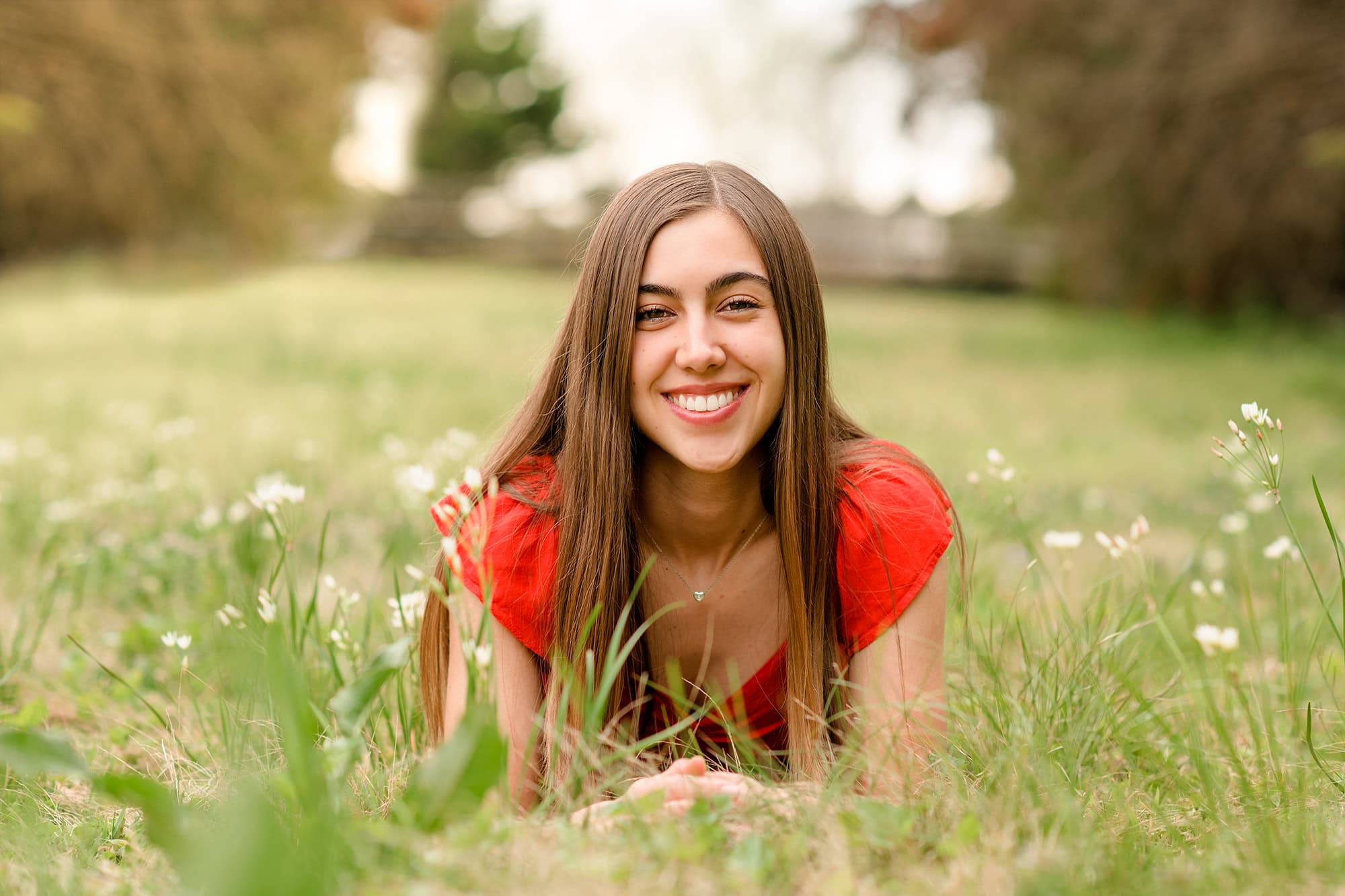 girl with dark hair wearing red shirt lays in green field