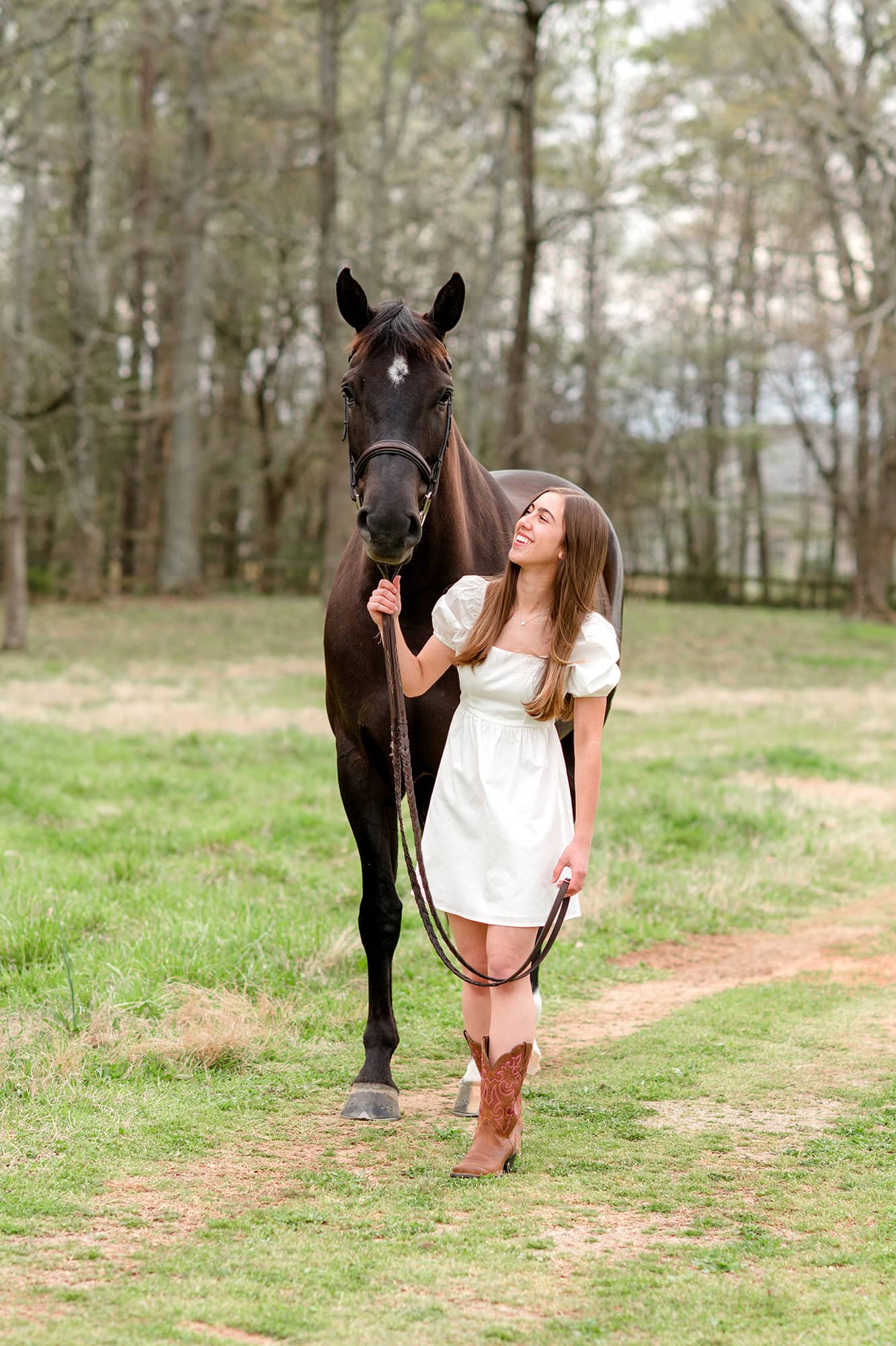 senior girl walks holding onto horses reigns in a charlotte area field