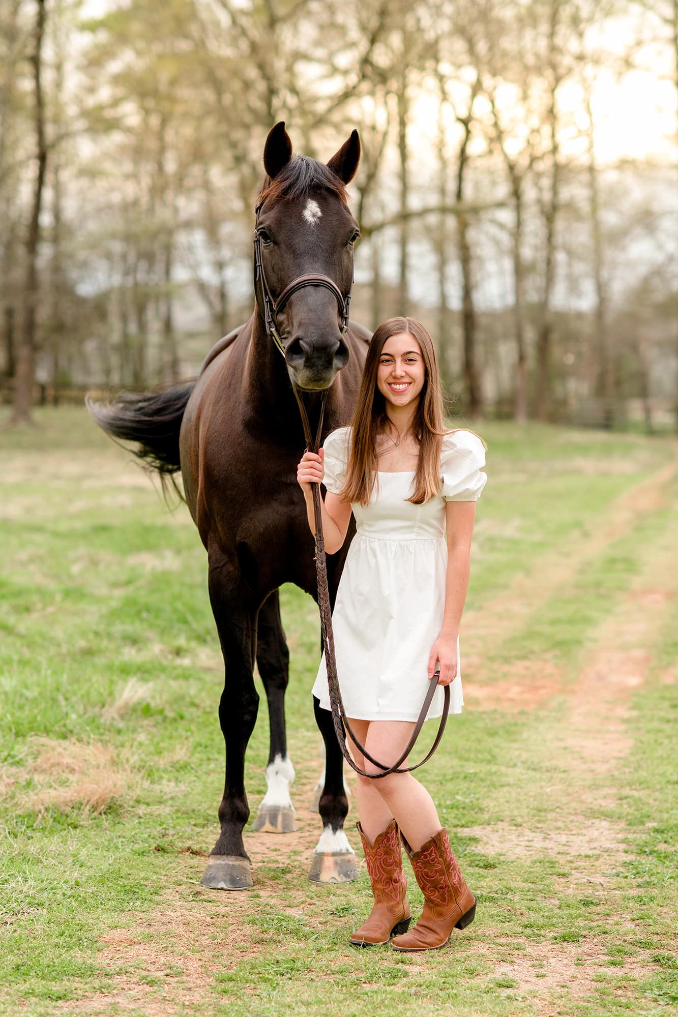 horse and dark hair charlotte area graduate stand in field pathway with girl holding reigns