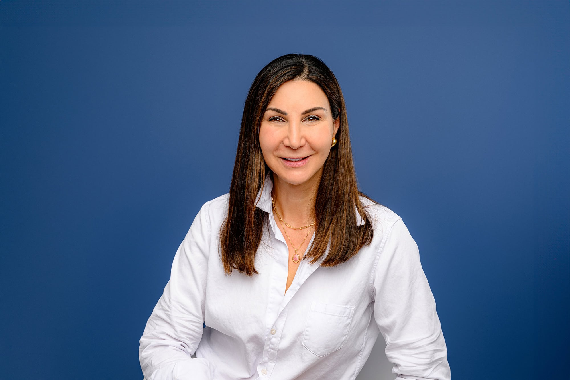 Charlotte artist in a white shirt on a blue background for her studio headshots