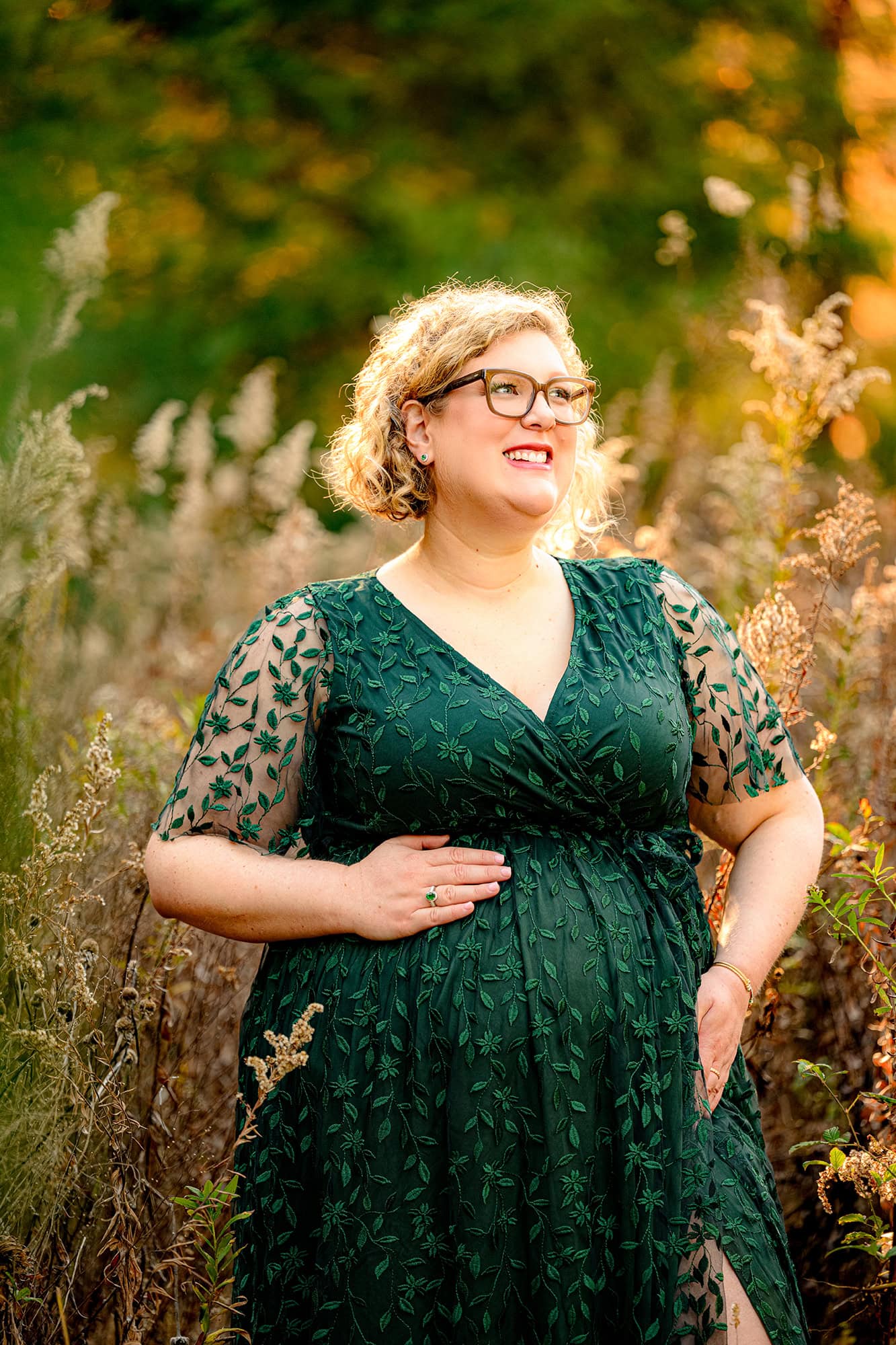 Charlotte area mother to be stands in a warm grassy field wearing a green dress during her photoshoot