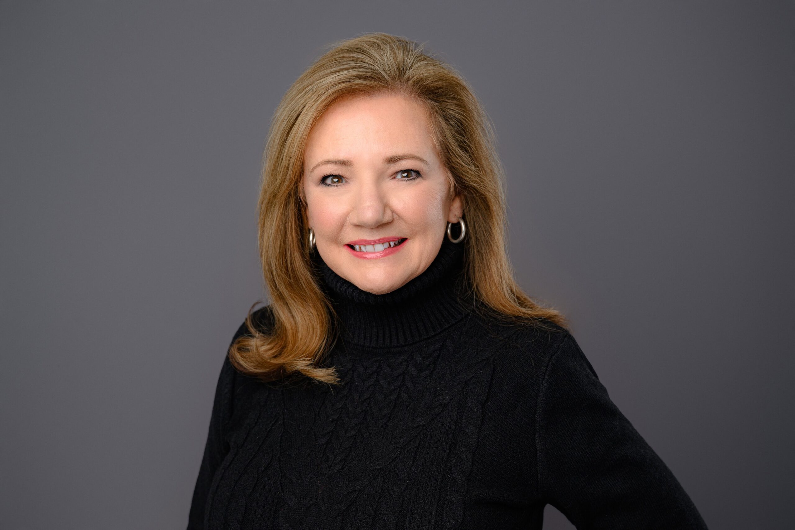 woman with blonde hair wearing a black turtleneck for her charlotte headshot session on a grey background