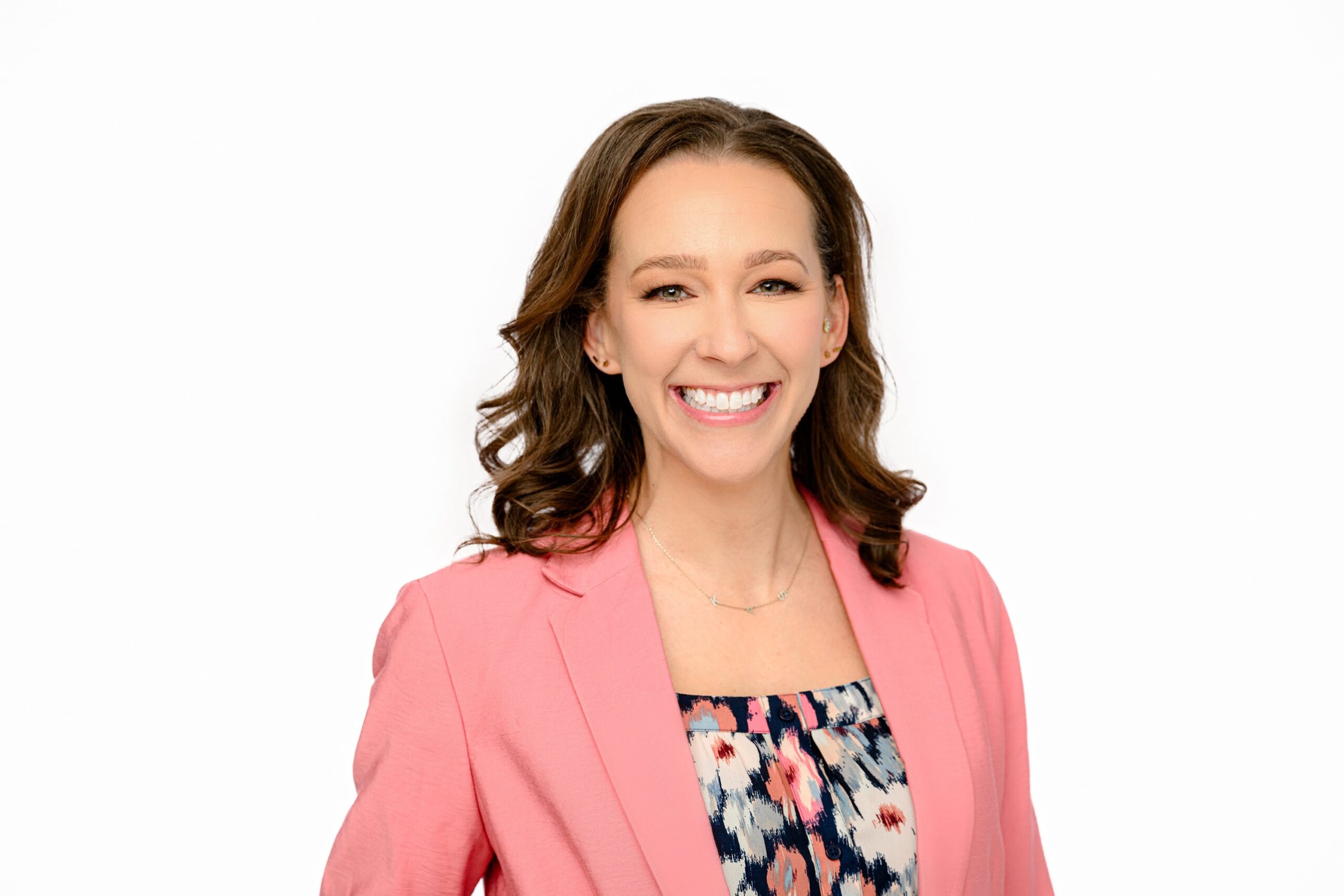 charlotte woman wearing a pink blazer and floral top with dark hair on a white background