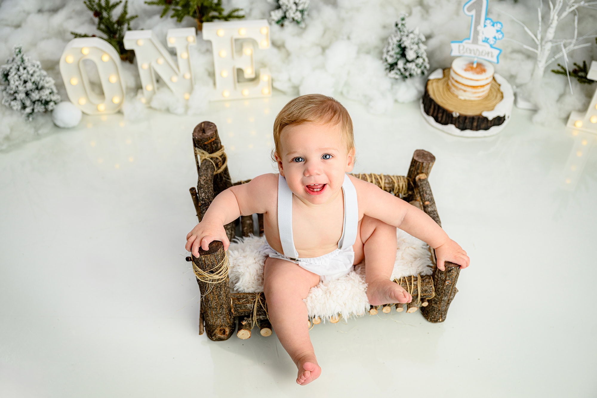 looking down on a little boy sitting on a log bed during his winter onederland cake smash session before smashing his cake