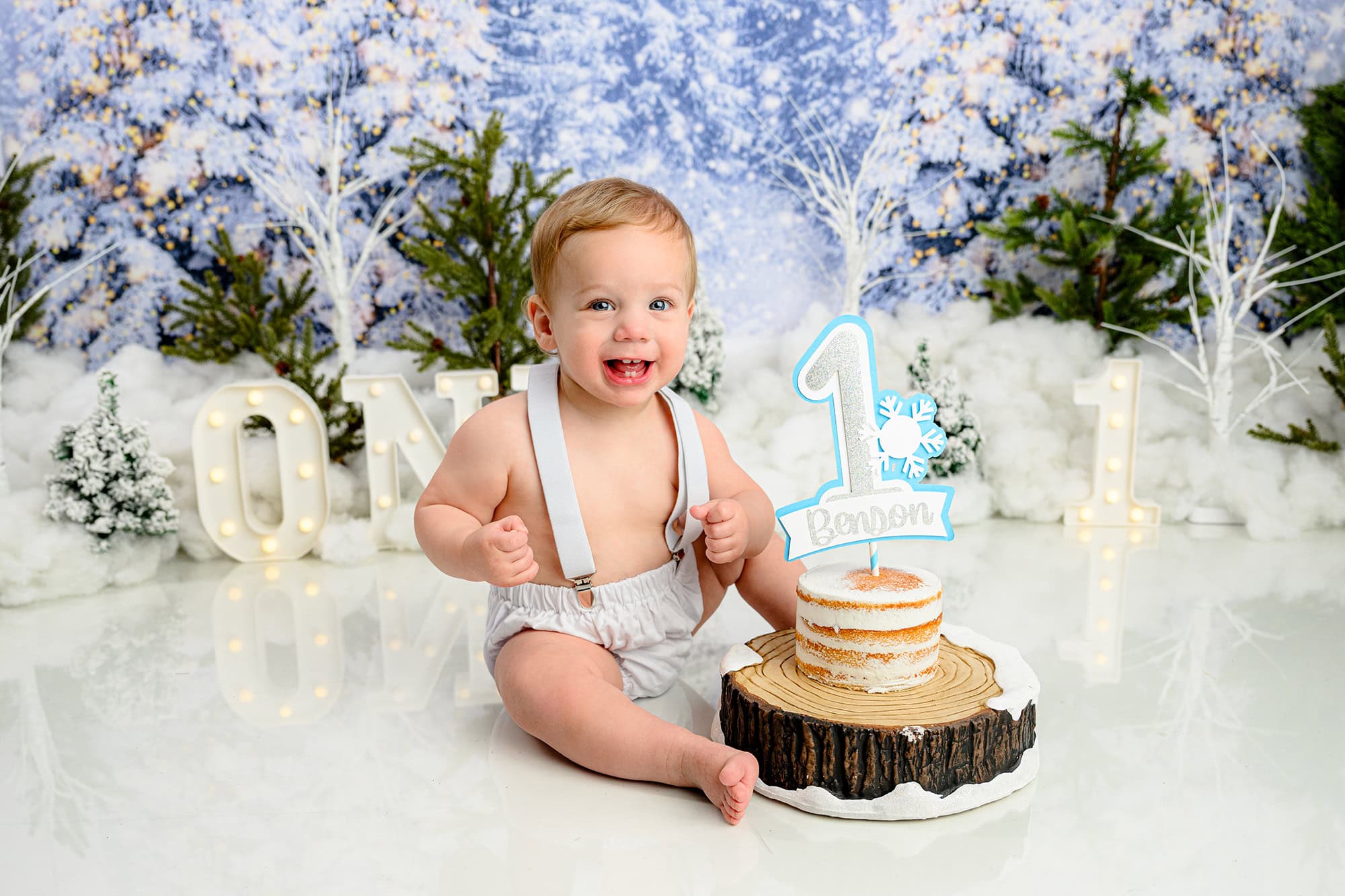 little blonde boy sits next to his winter onederland cake during his birthday photo session