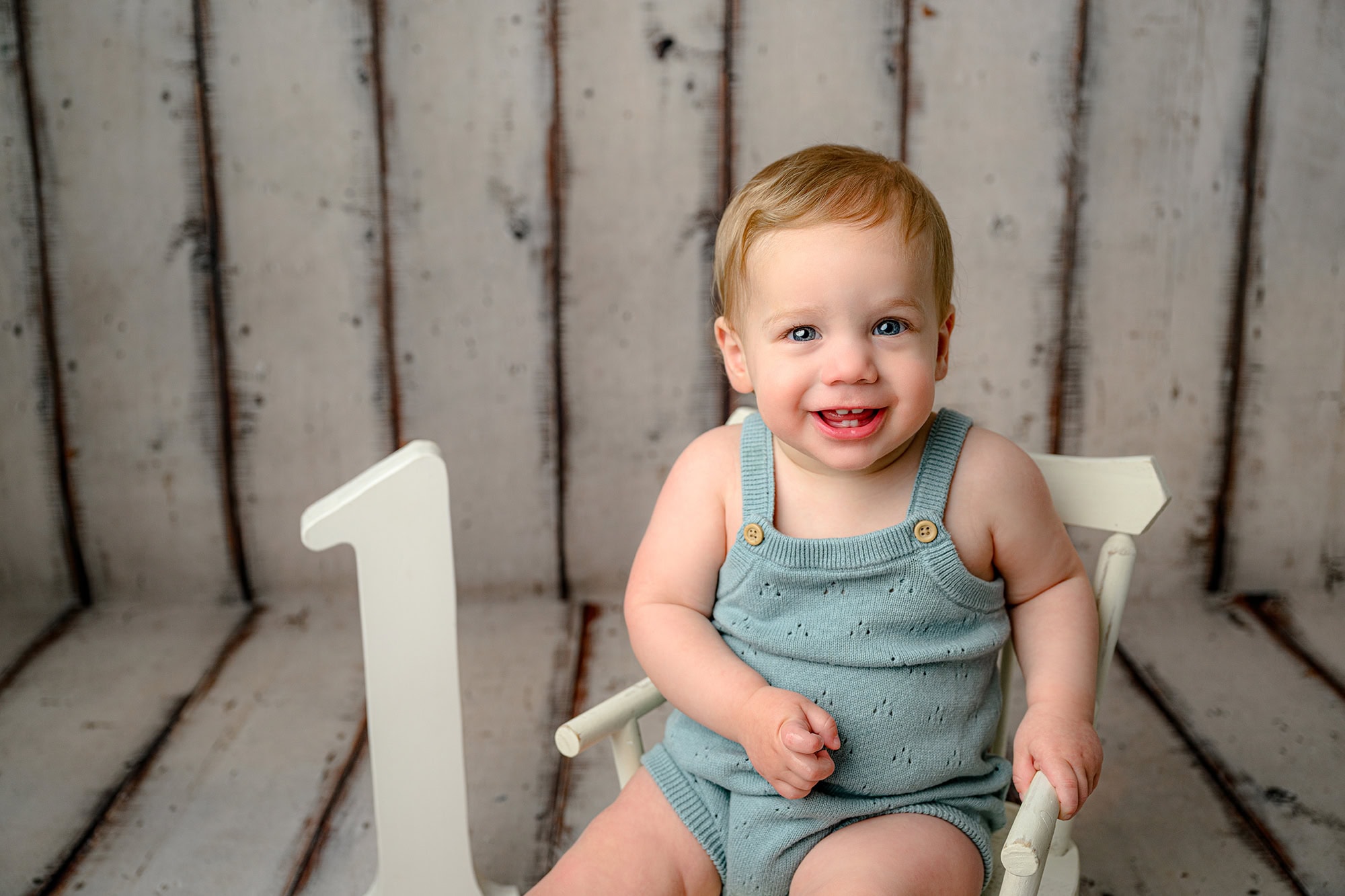 Blue eyed charlotte baby in his milestone set wearing a blue romper sitting in a chair