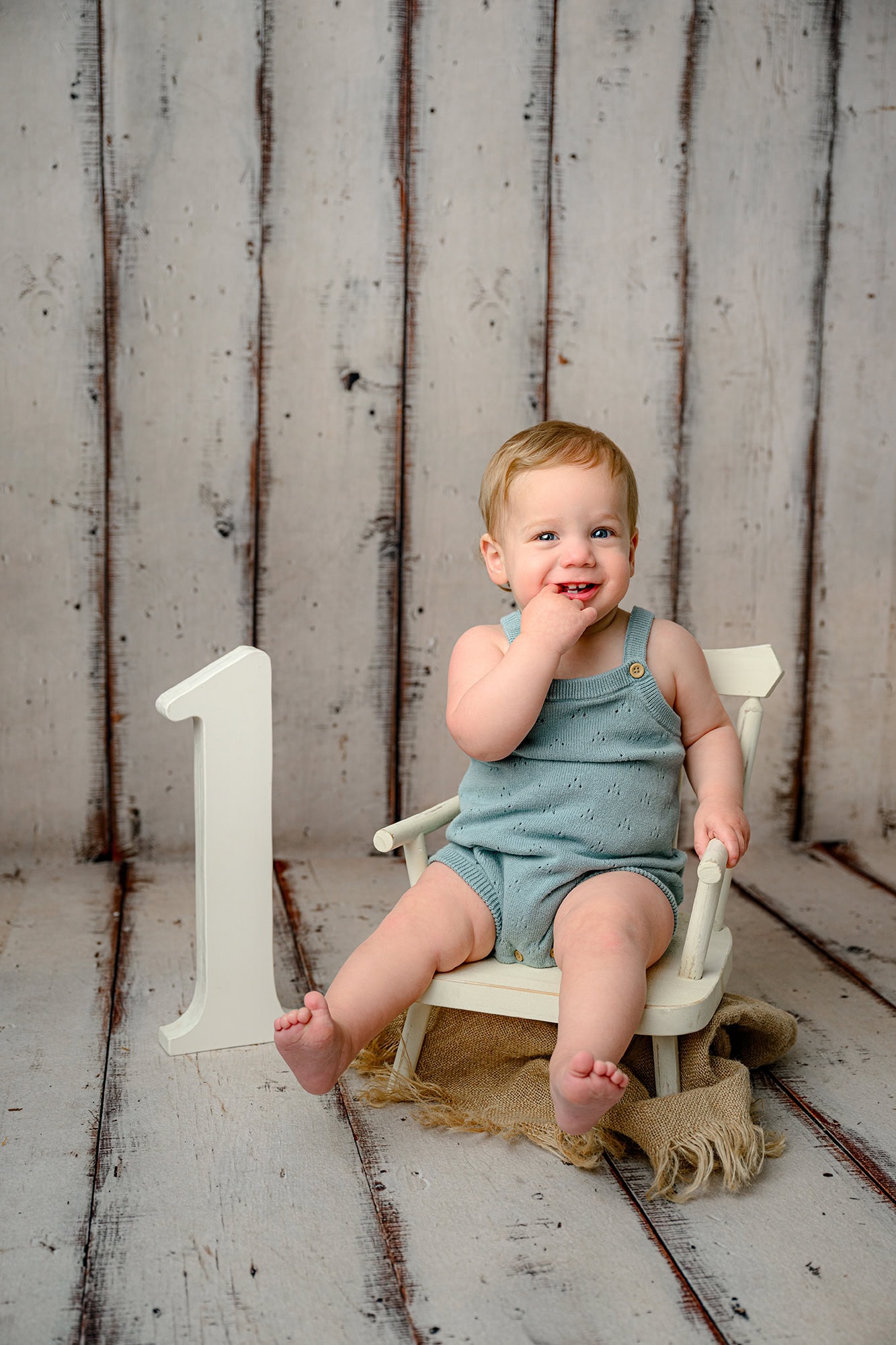 little boy giggles with his hand in his mouth during his milestone photos