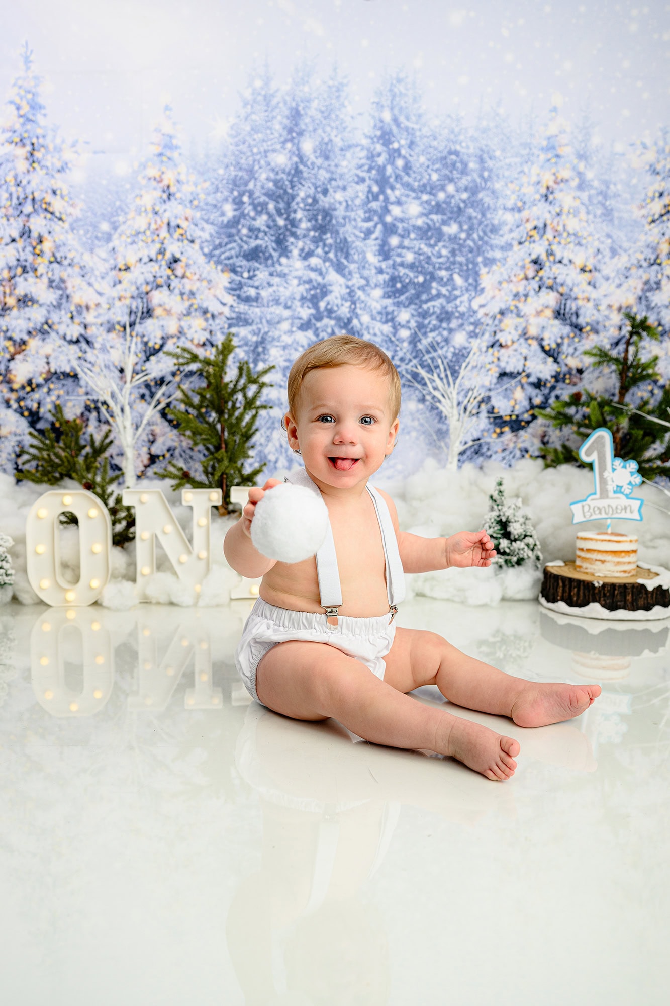 Charlotte cake smash photo of winter adventure scene with little one holding a snowball in his winter onederland set
