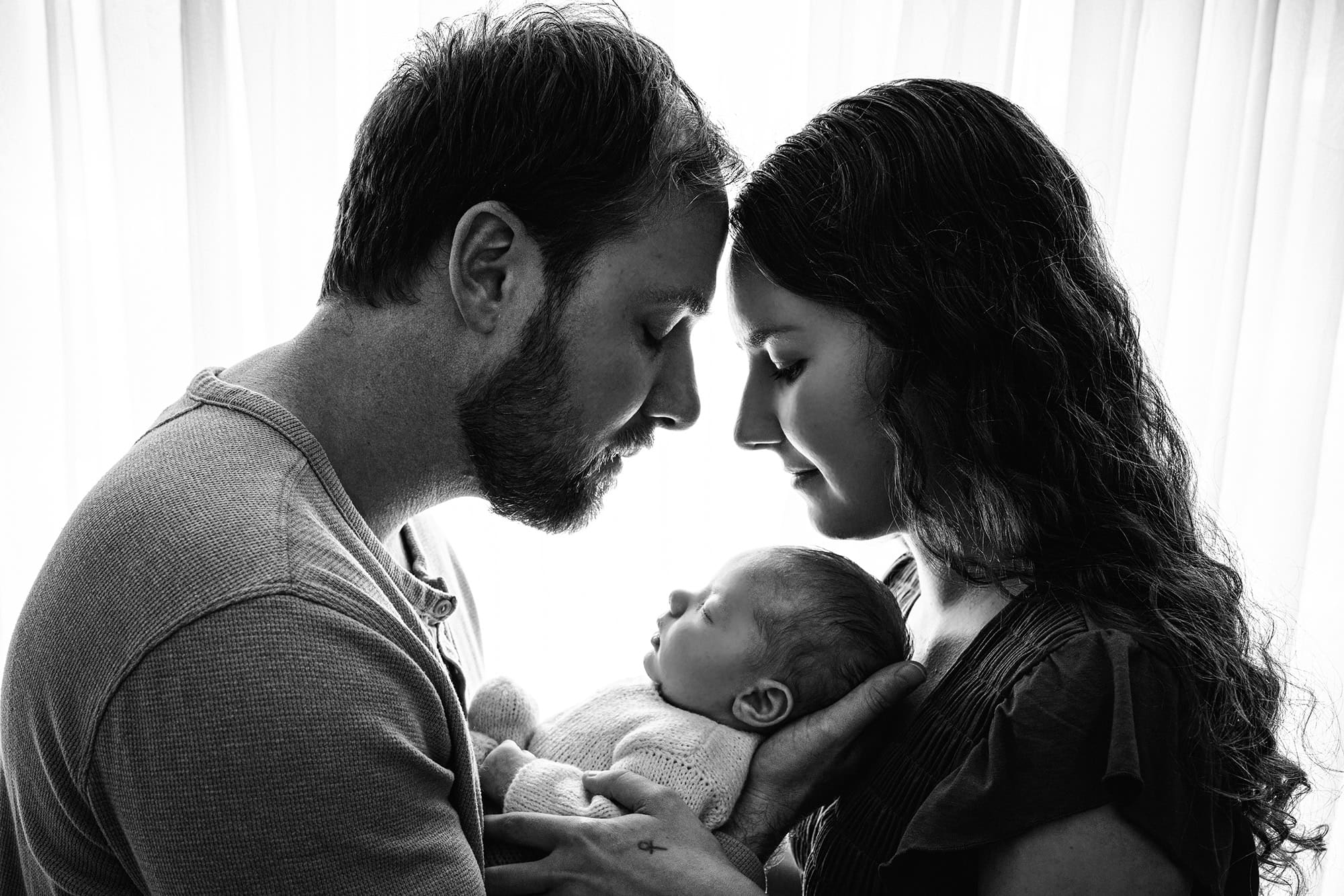 black and white photo of winter newborn photography session with parents holding their baby between them
