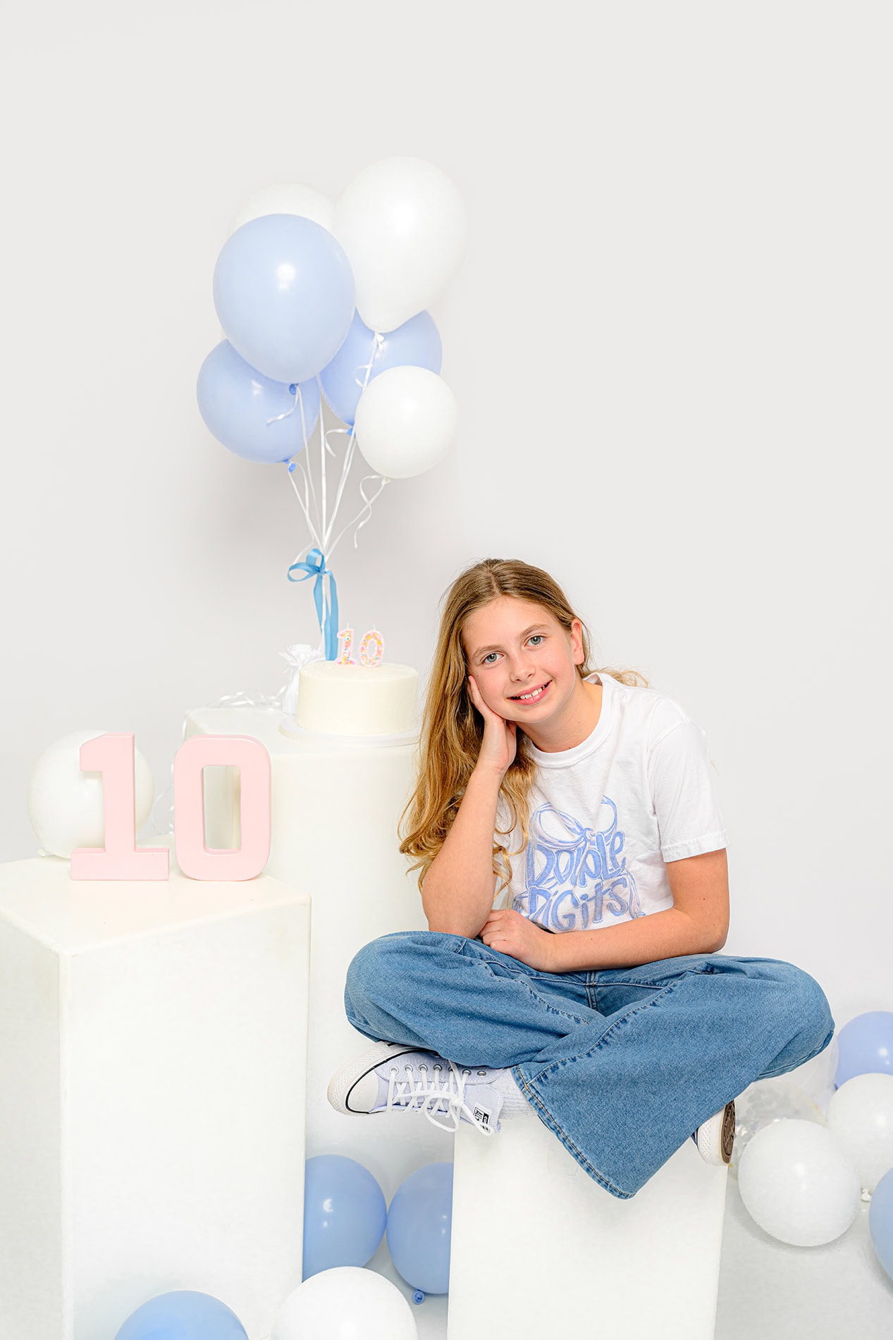 little girl leaning on her hand sitting criss cross with ten year birthday balloons and decorations around her