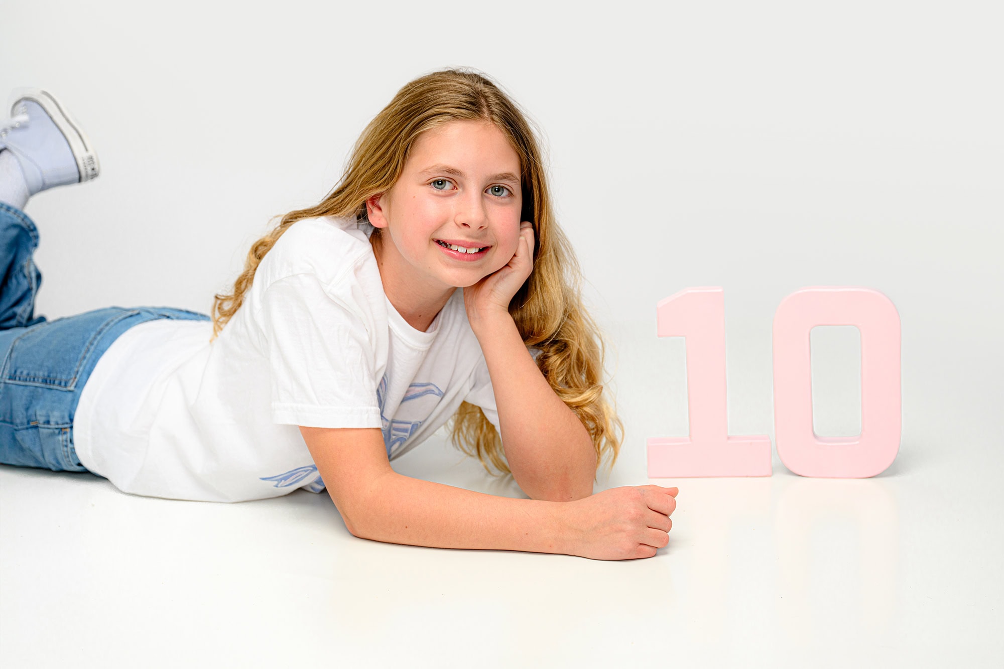 10 year old photo session of child wearing a t shirt and jeans with two pink numbers beside her while she lays on her belly
