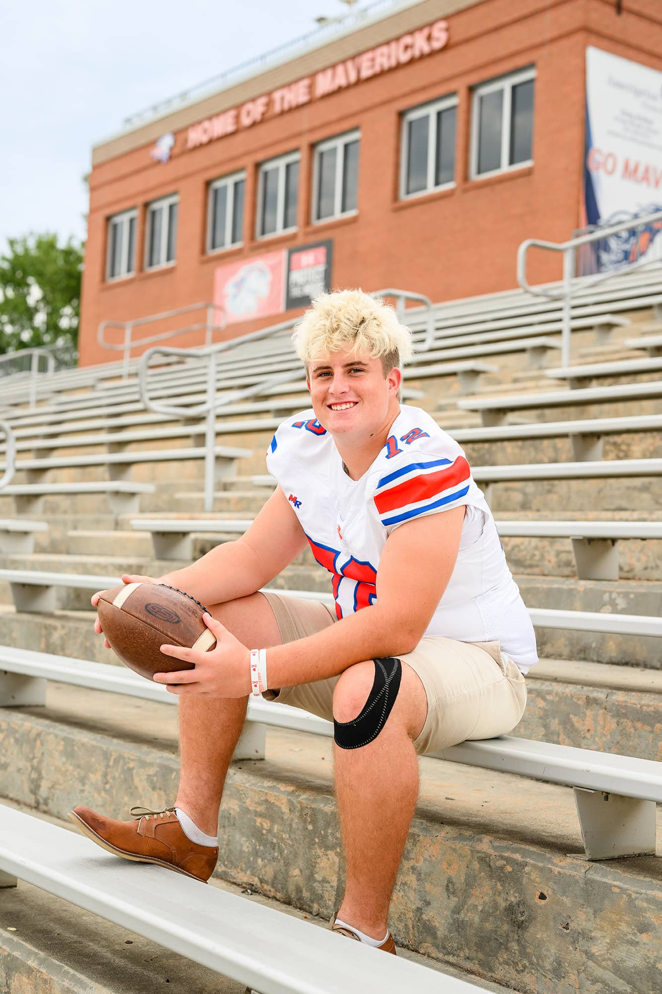 senior at marvin ridge high school sitting in stadium wearing his jersey holding a football