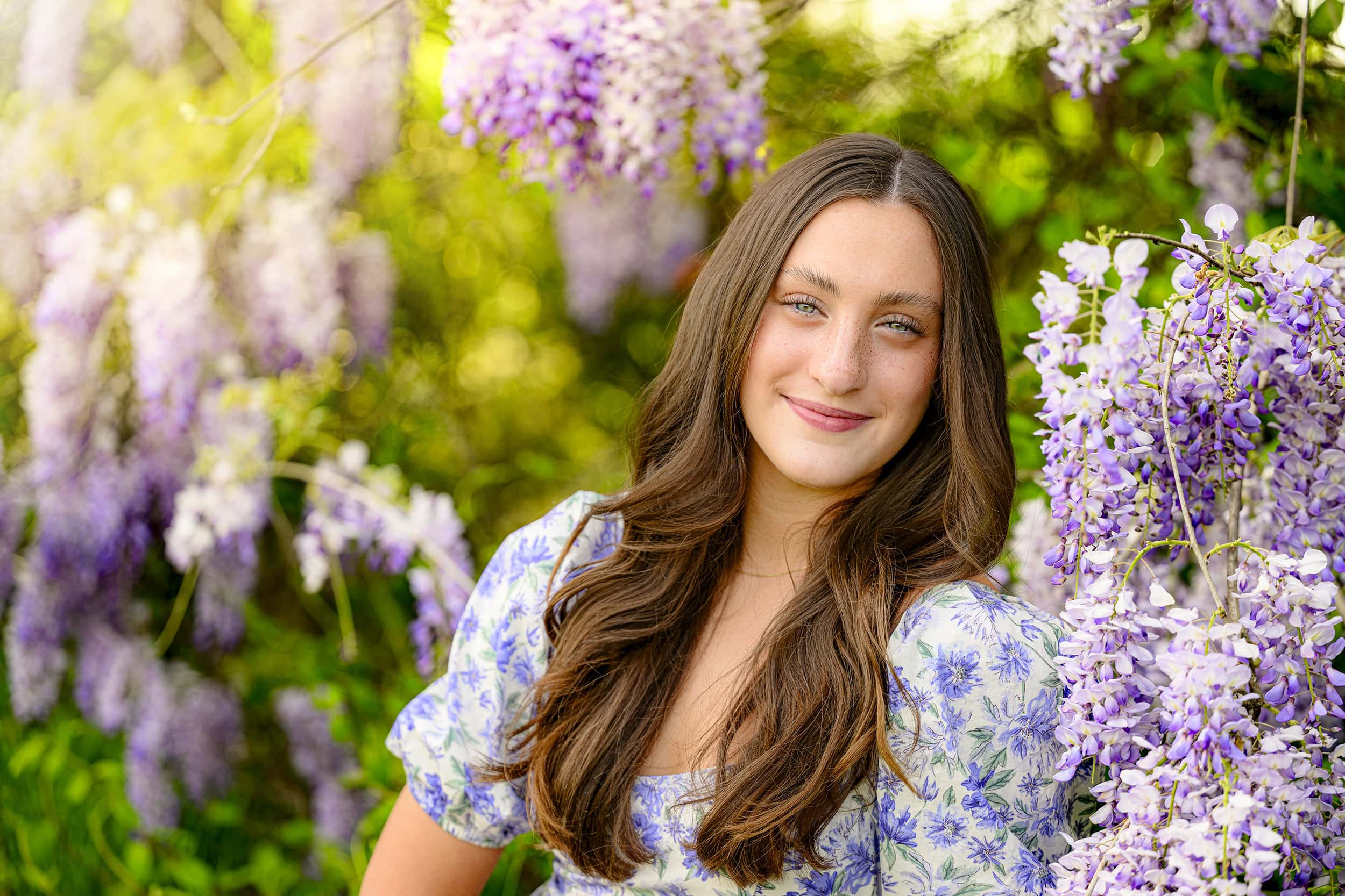 charlotte catholic senior is wearing a blue and purple floral dress framed by wisteria in this charlotte location