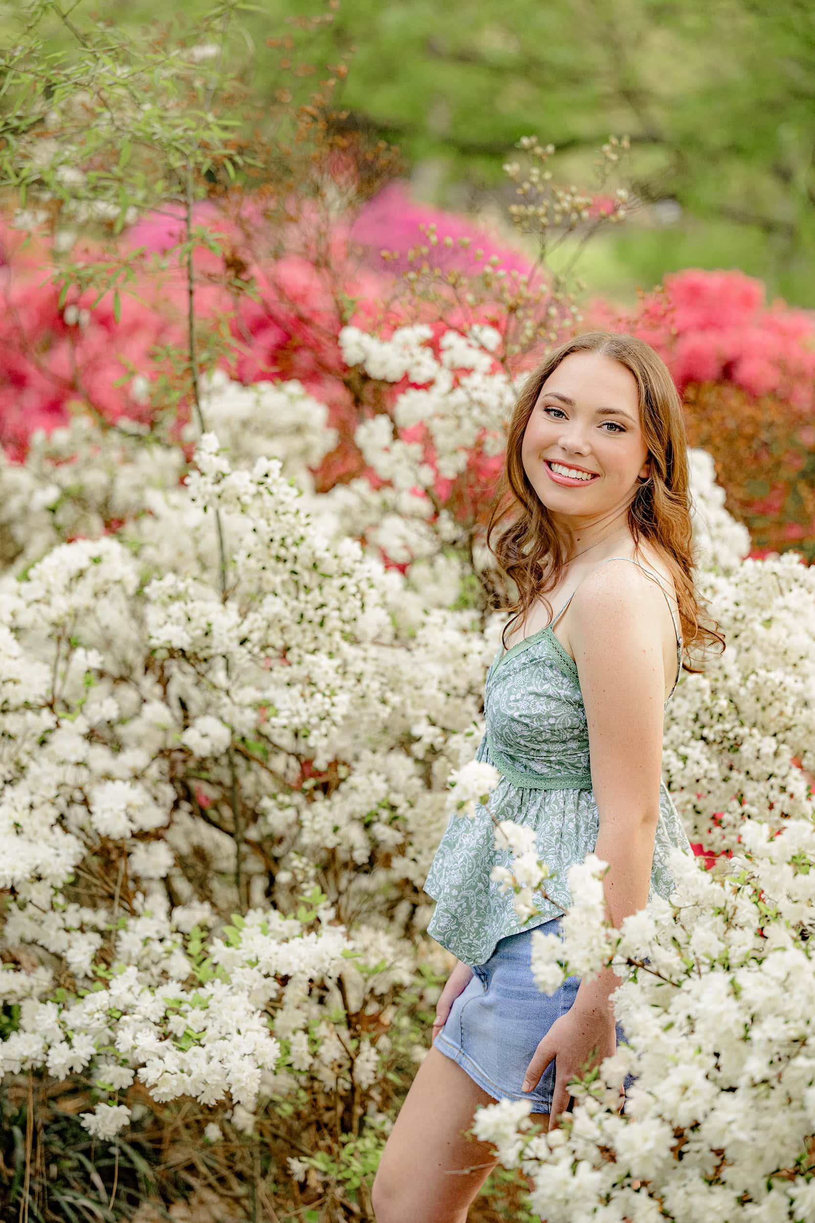 senior turns and looks over her shoulder during photo surrounded by azelea blooms