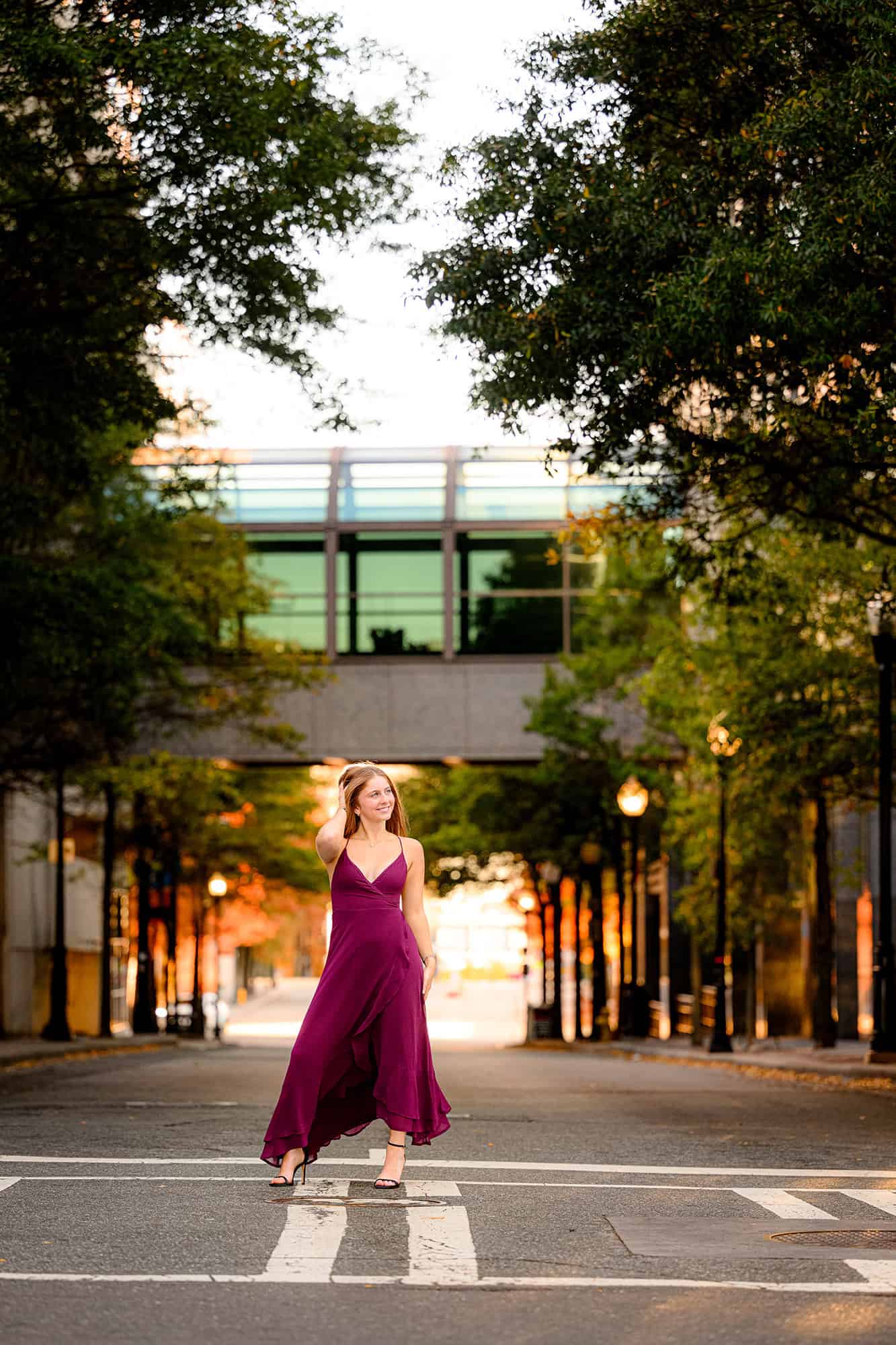 uptown charlotte location with grad standing in a street wearing a cranberry dress for her senior portraits