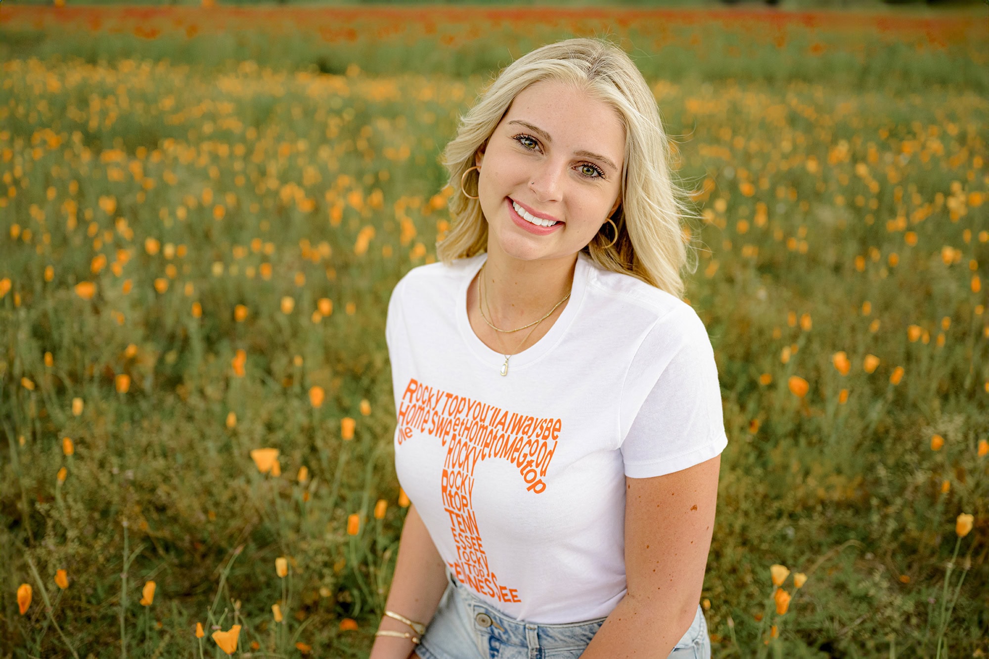 blonde grad wearing white UT shirt while sitting in a flower field