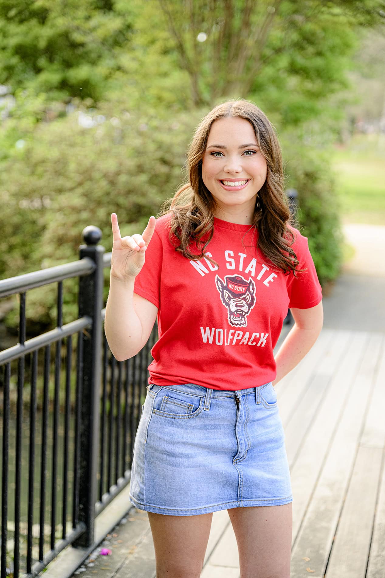dark hair senior wearing a red shirt and doing the handmotion for her future college