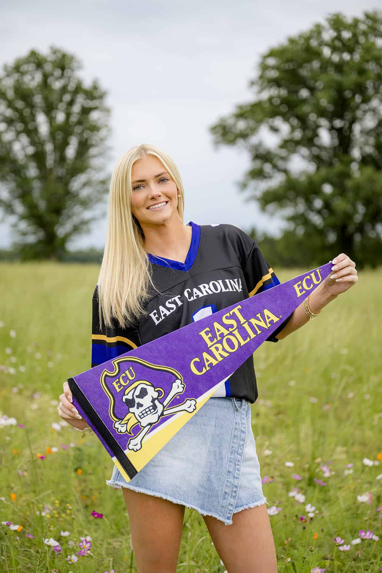 blonde senior wearing college jersey and holding her ECU college gear pennant