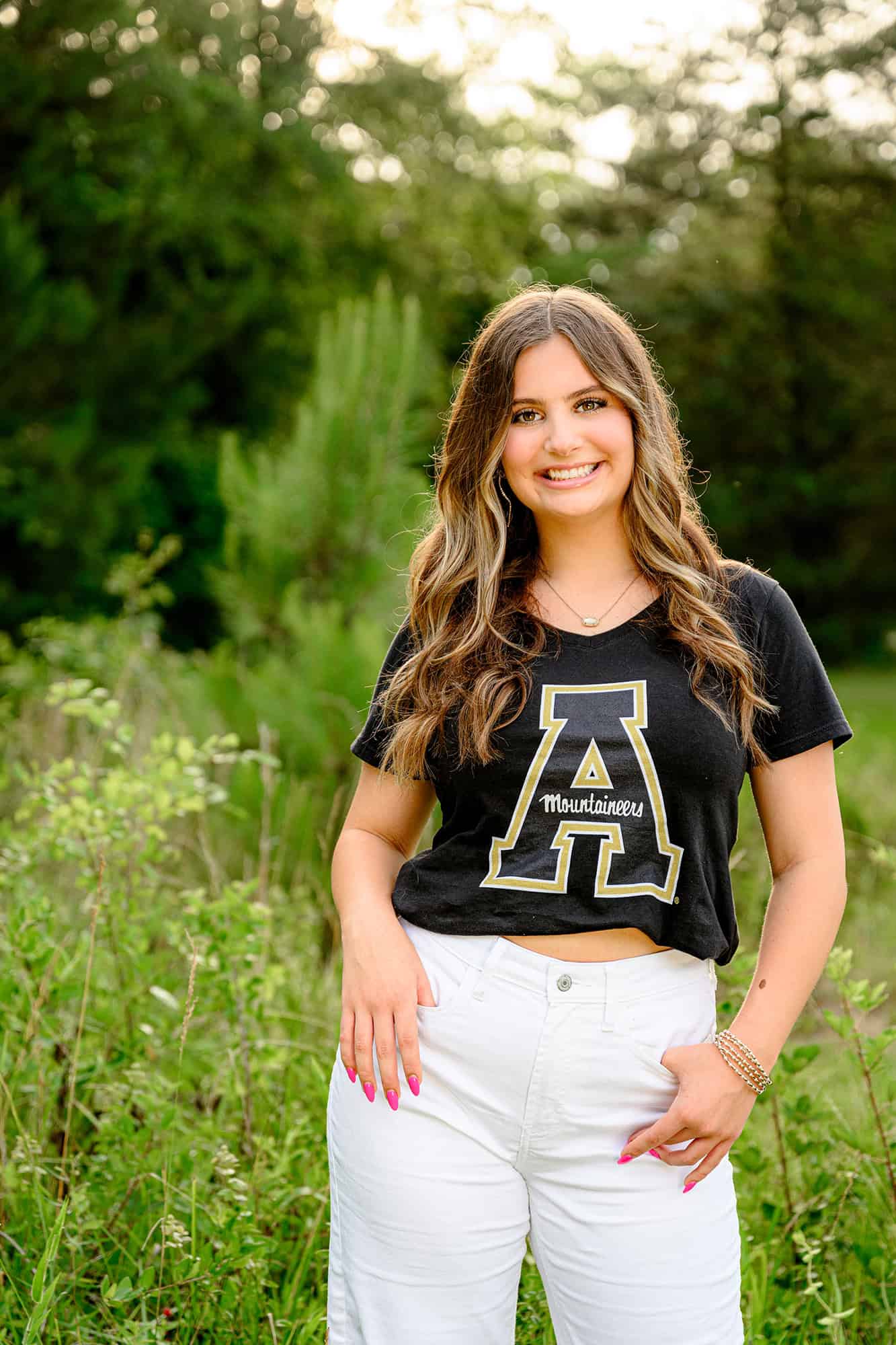 dark hair grad wearing black app state t shirt and white jeans 