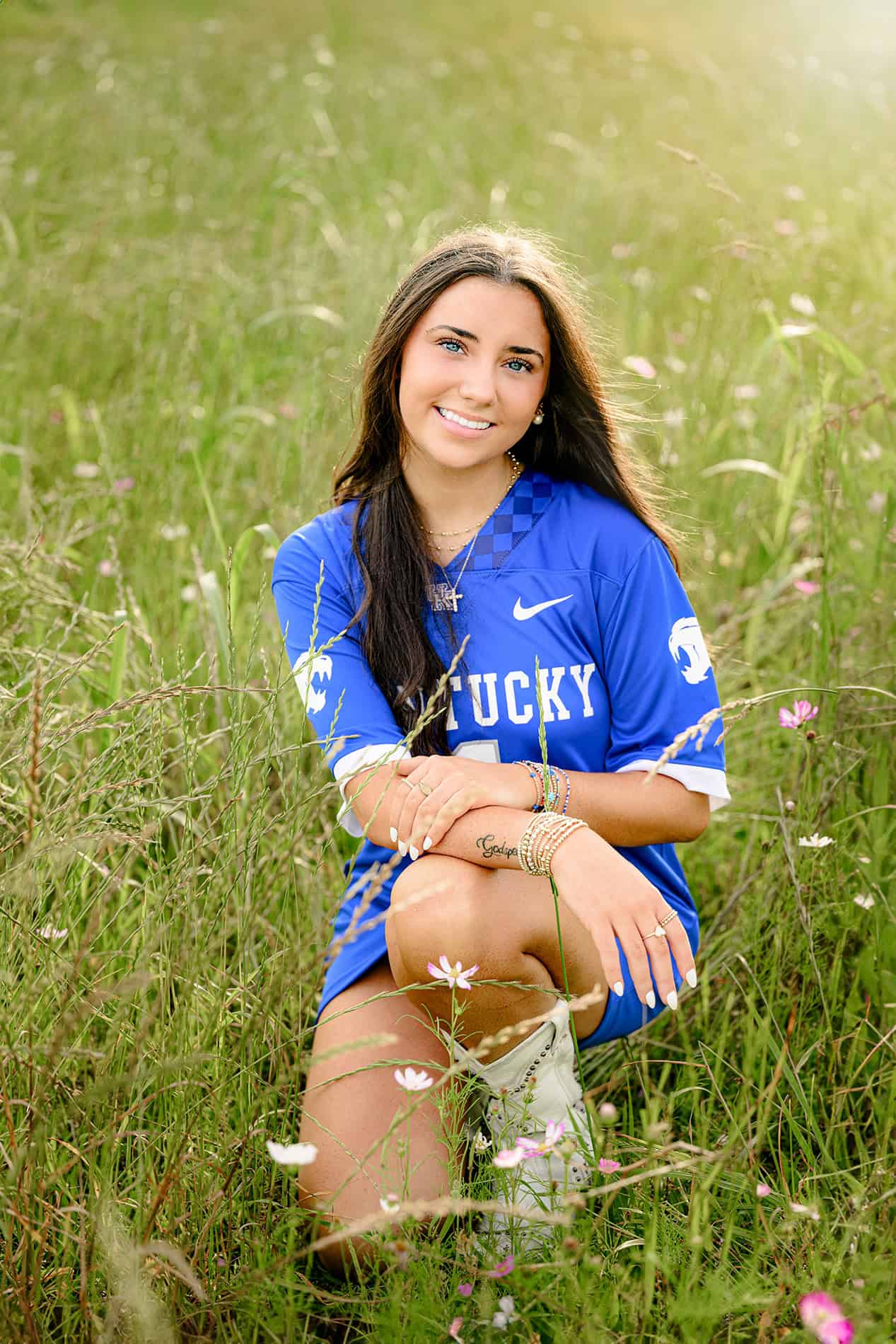 dark hair future university of kentucky student kneeling in flower field in blue jersey