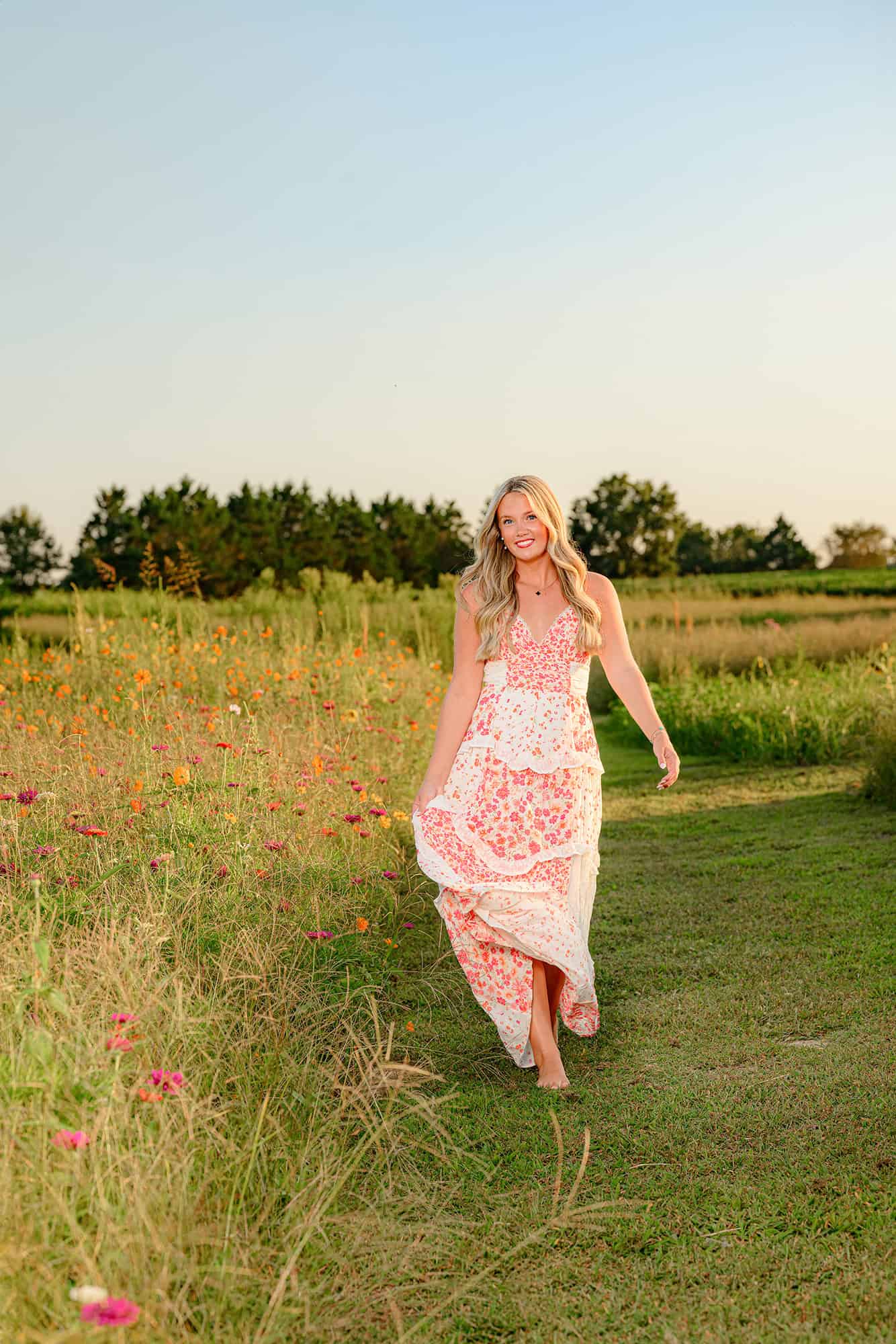 blonde charlotte senior smiles as she walks barefoot through a flower field in south charlotte