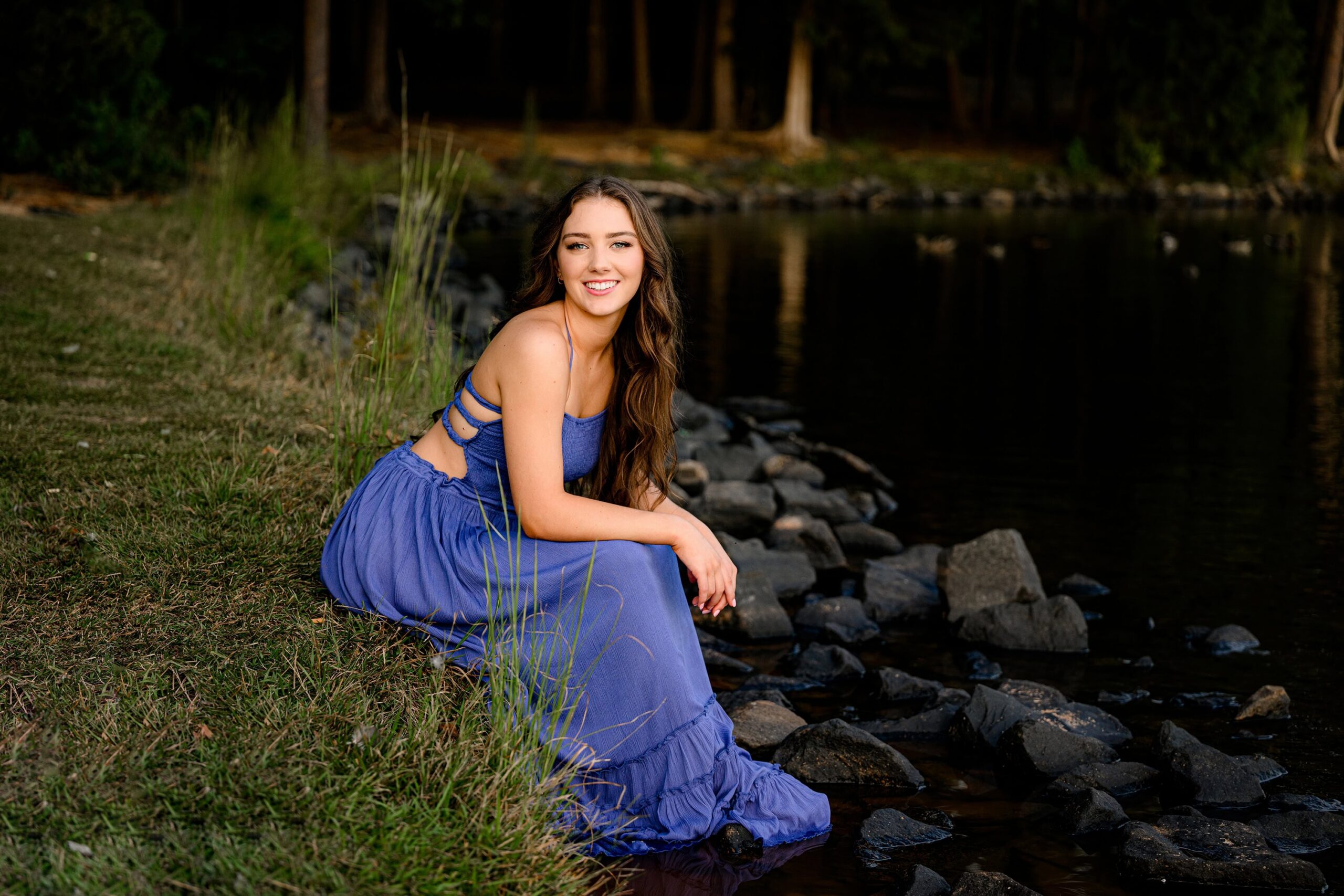 charlotte area senior sitting on bank of pond in blue dress for senior photos