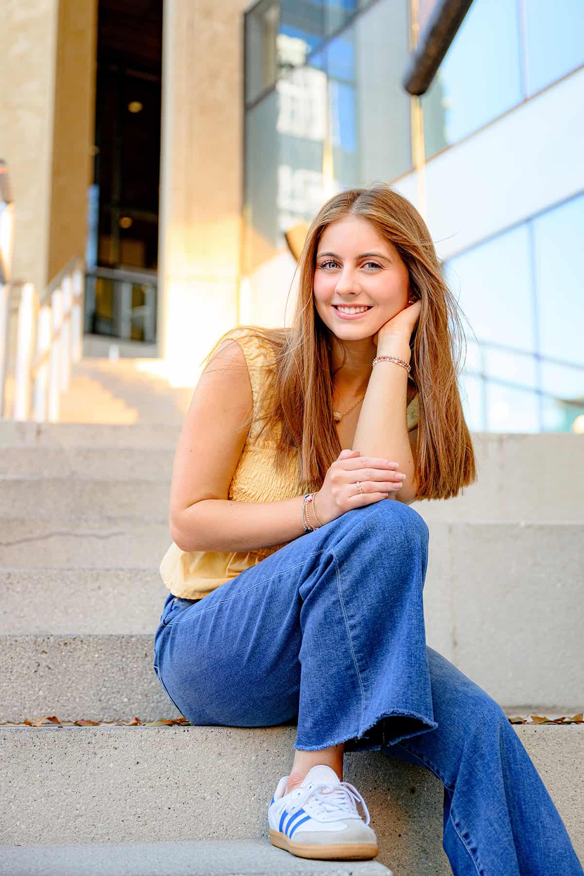 senior sits in jeans, yellow top, and sneakers with on the steps in uptown charlotte