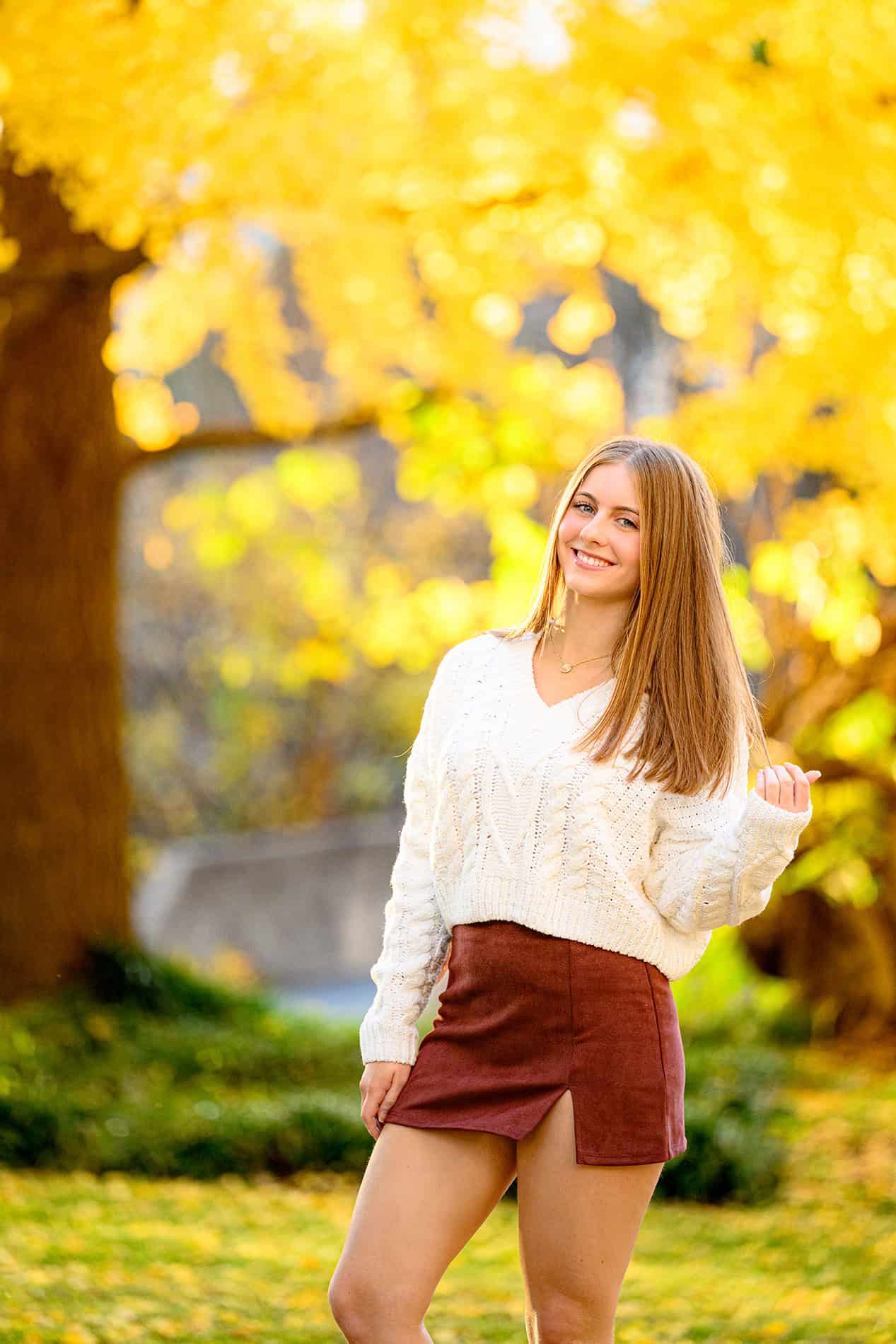 uptown charlotte senior photo of grad in white sweater and skirt with yellow park trees behind her 