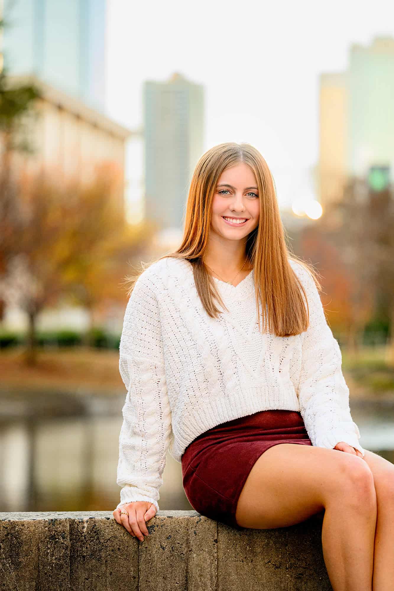 uptown graduate session with charlotte senior dressed in cream sweater and skirt with skyline behind her