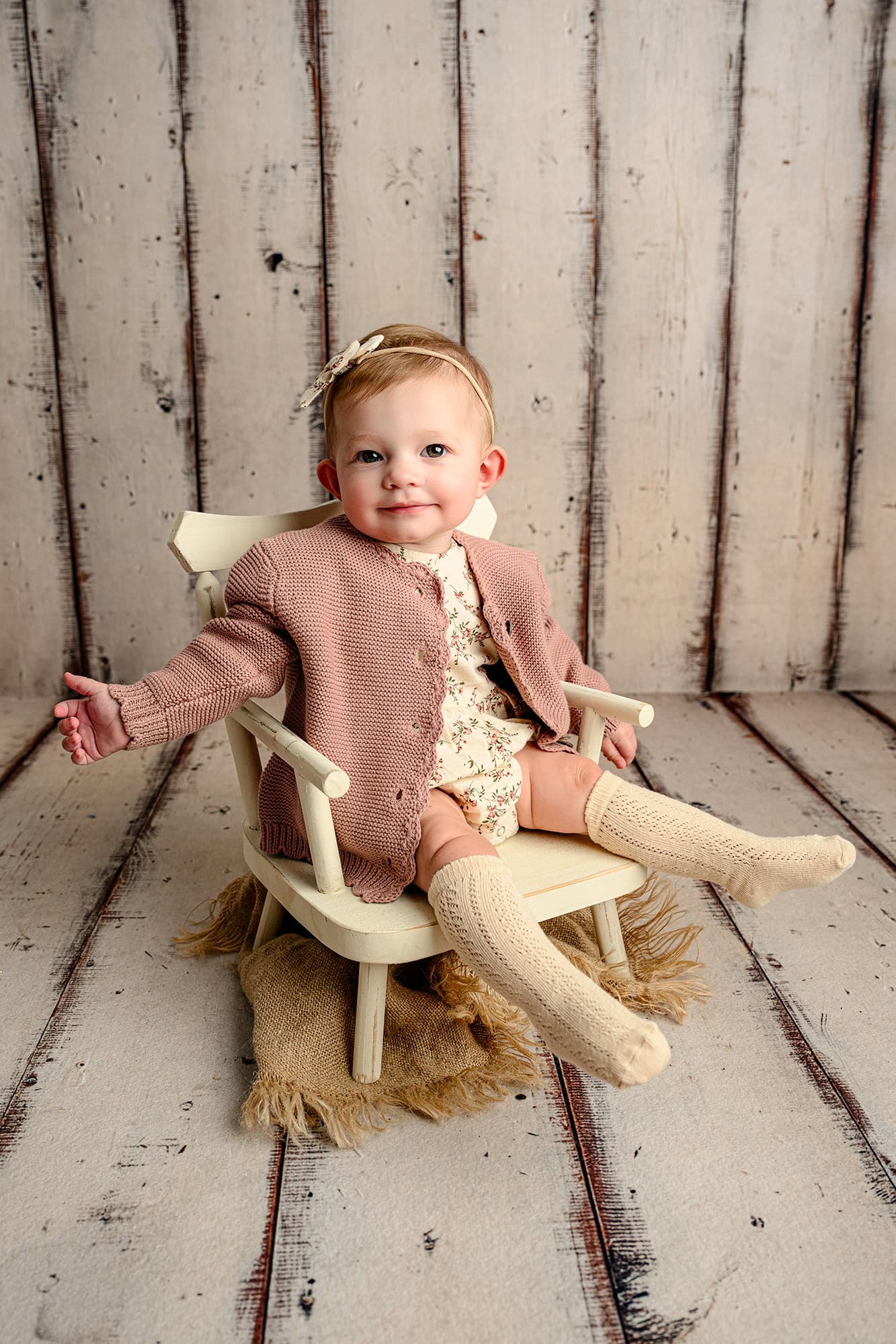7 month old girl sits in chair wearing. a floral romper for her styled photo session