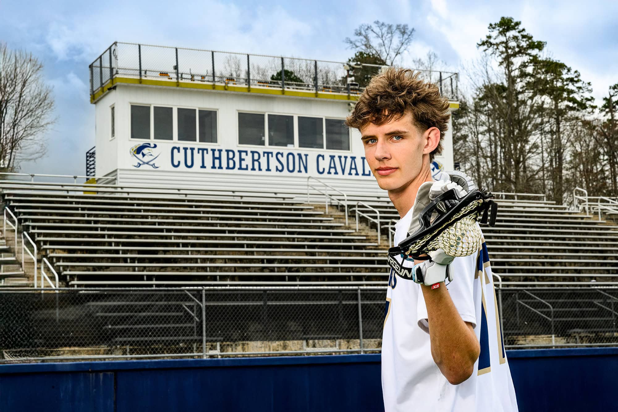 charlotte lacrosse player holding his stick behind his shoulders with school stadium behind him