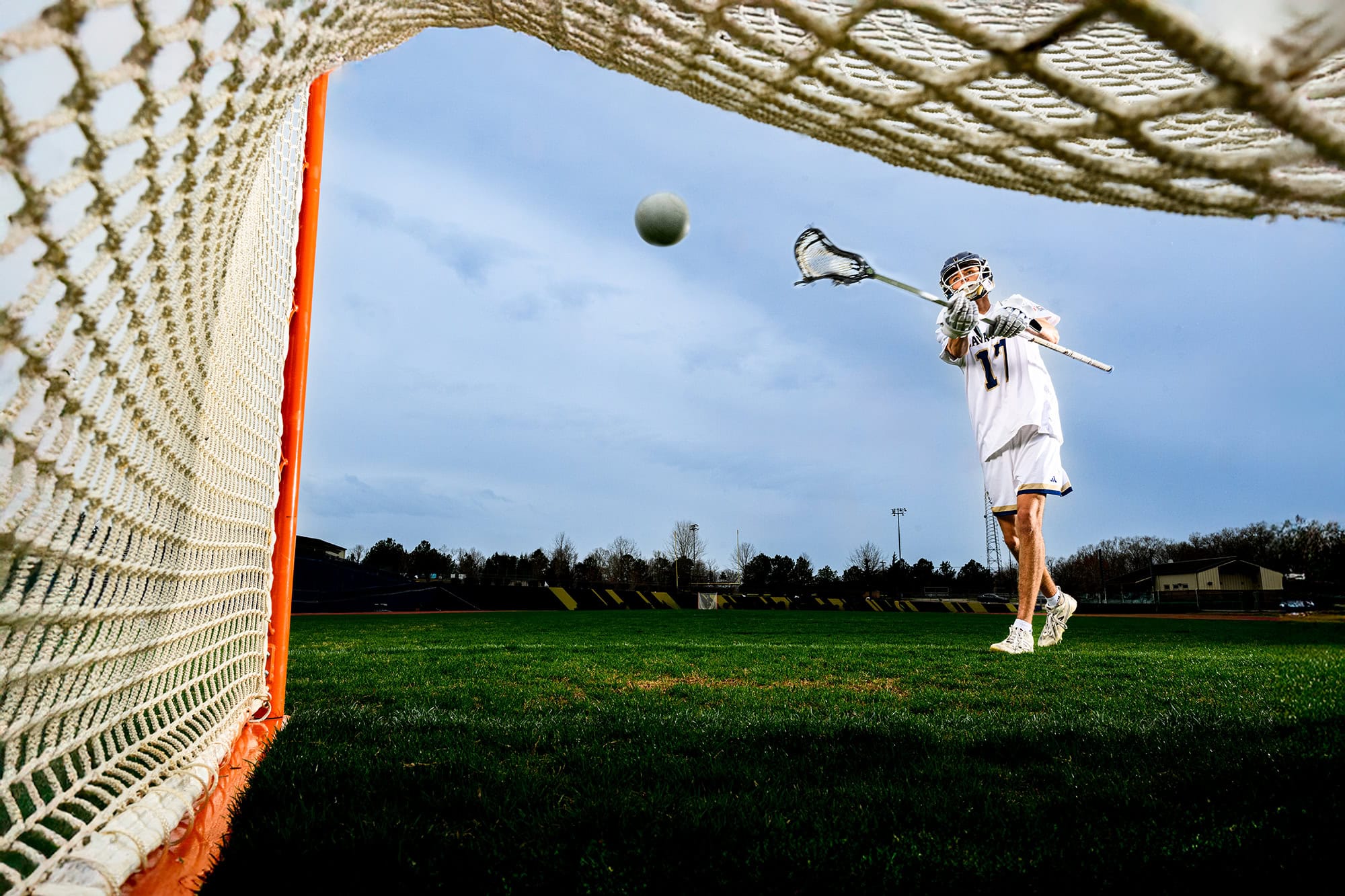 charlotte senior lacrosse player shooting a goal into a lacrosse net during his sports photos