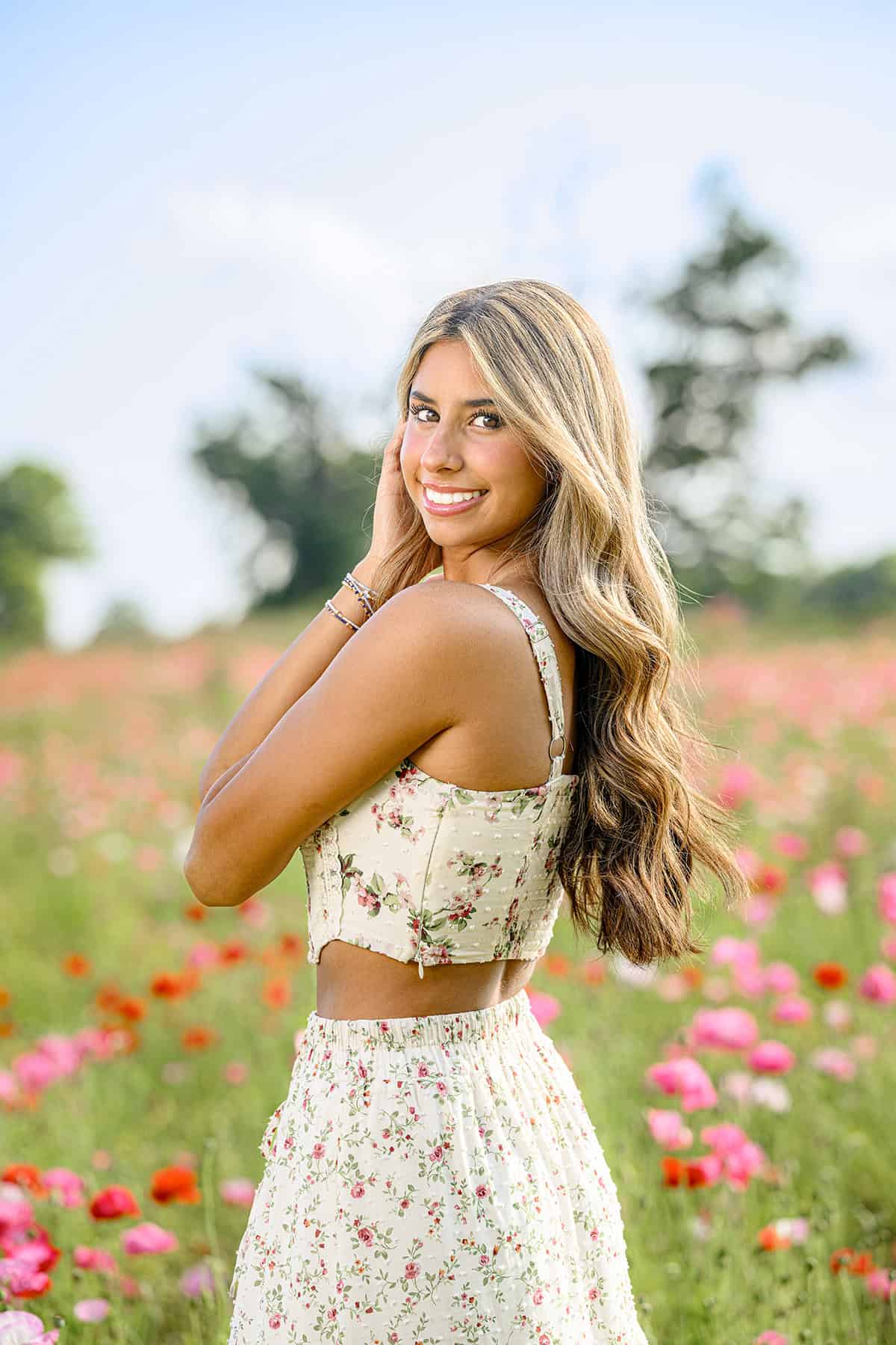 charlotte grad standing in pink poppy field wearing a pink and cream floral dress