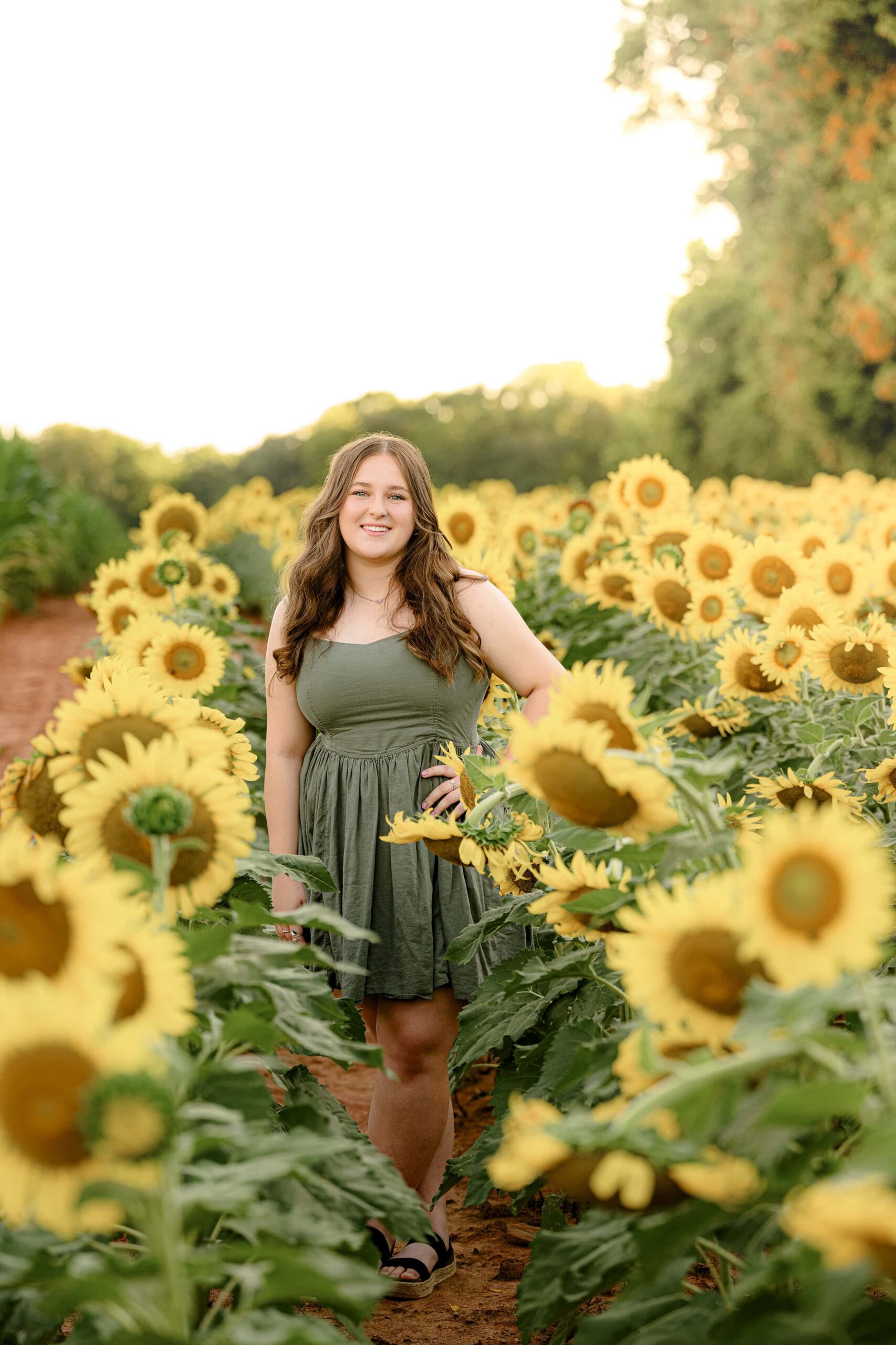 dark hair grad stands in green dress in a wildflower sunflower field