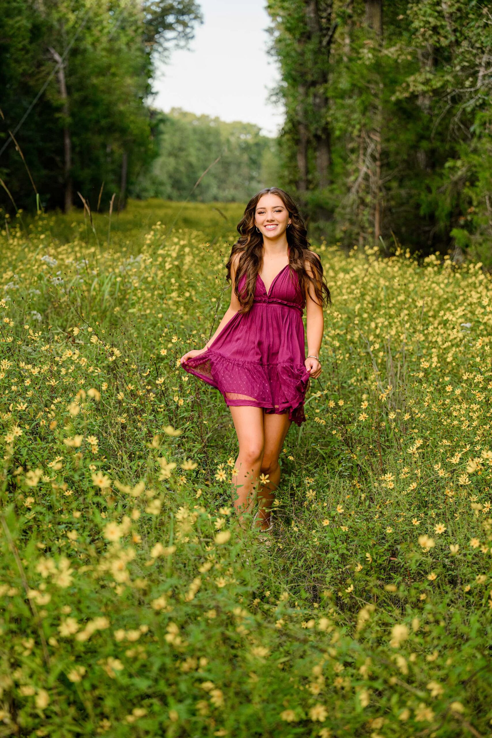 dark hair grad walking in yellow floral field wearing a short purple dress