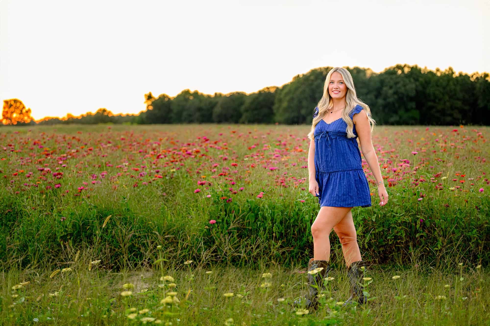 blonde senior wearing a blue dress in a pink zinnia wildflower field