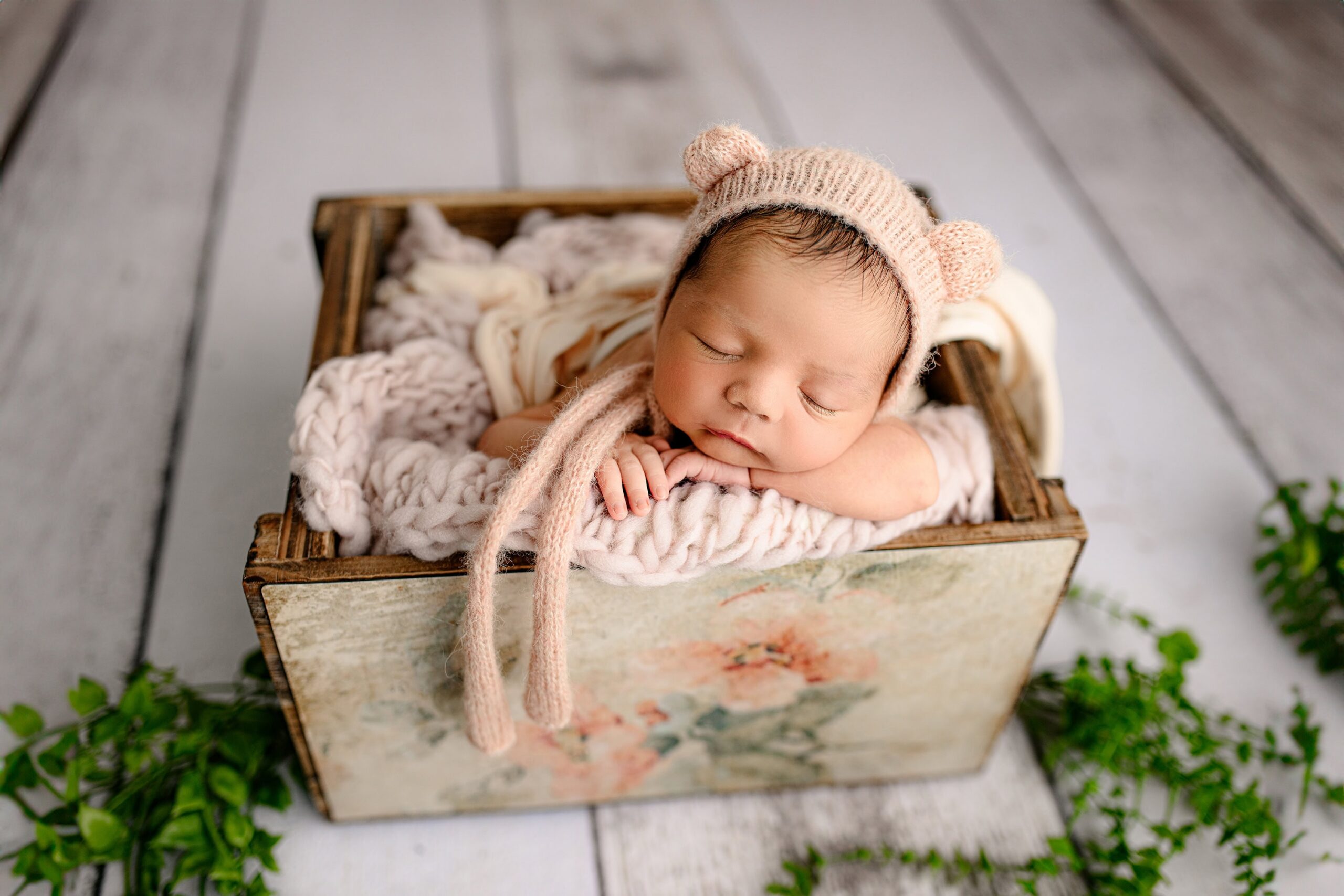 charlotte newborn girl wears a peach bear ear bonnet posed in a crate