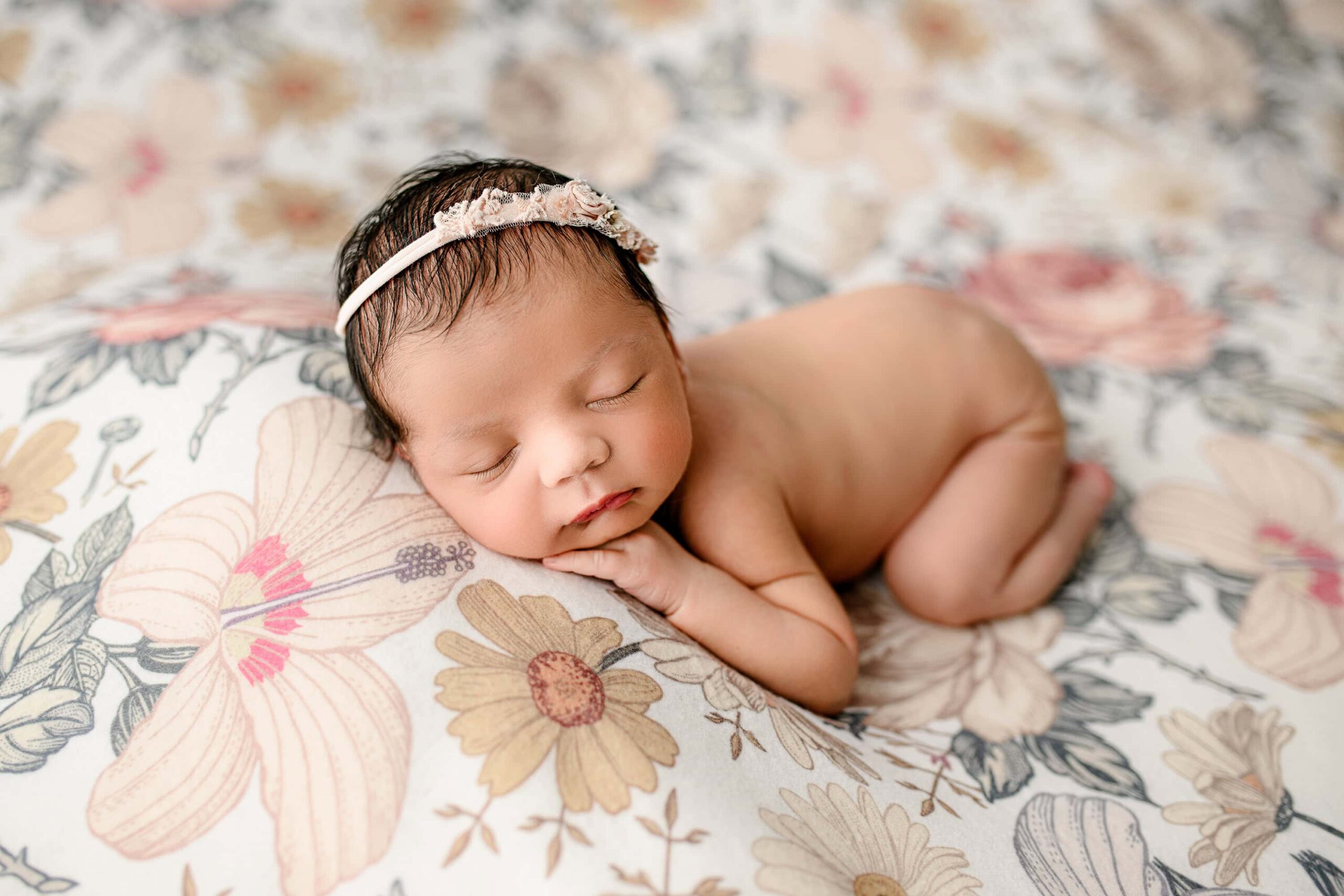 charlotte newborn girl posed on a floral background wearing a tiny headband