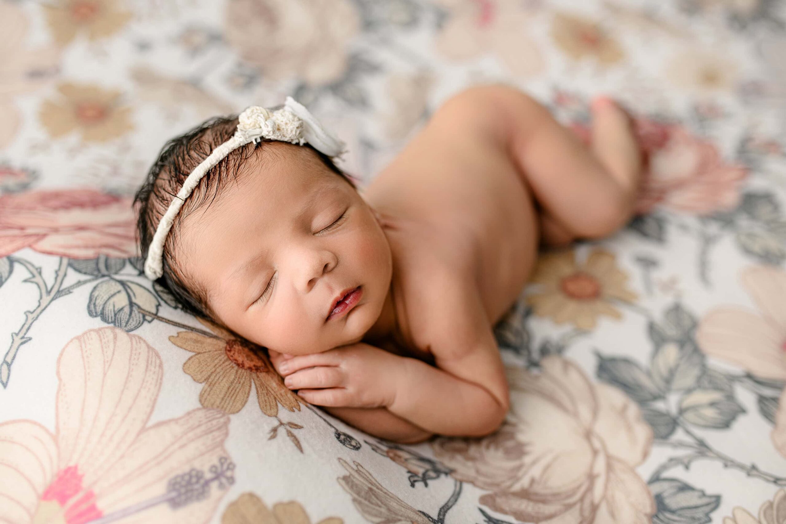 newborn girl is laying on her side while sleeping on a floral background