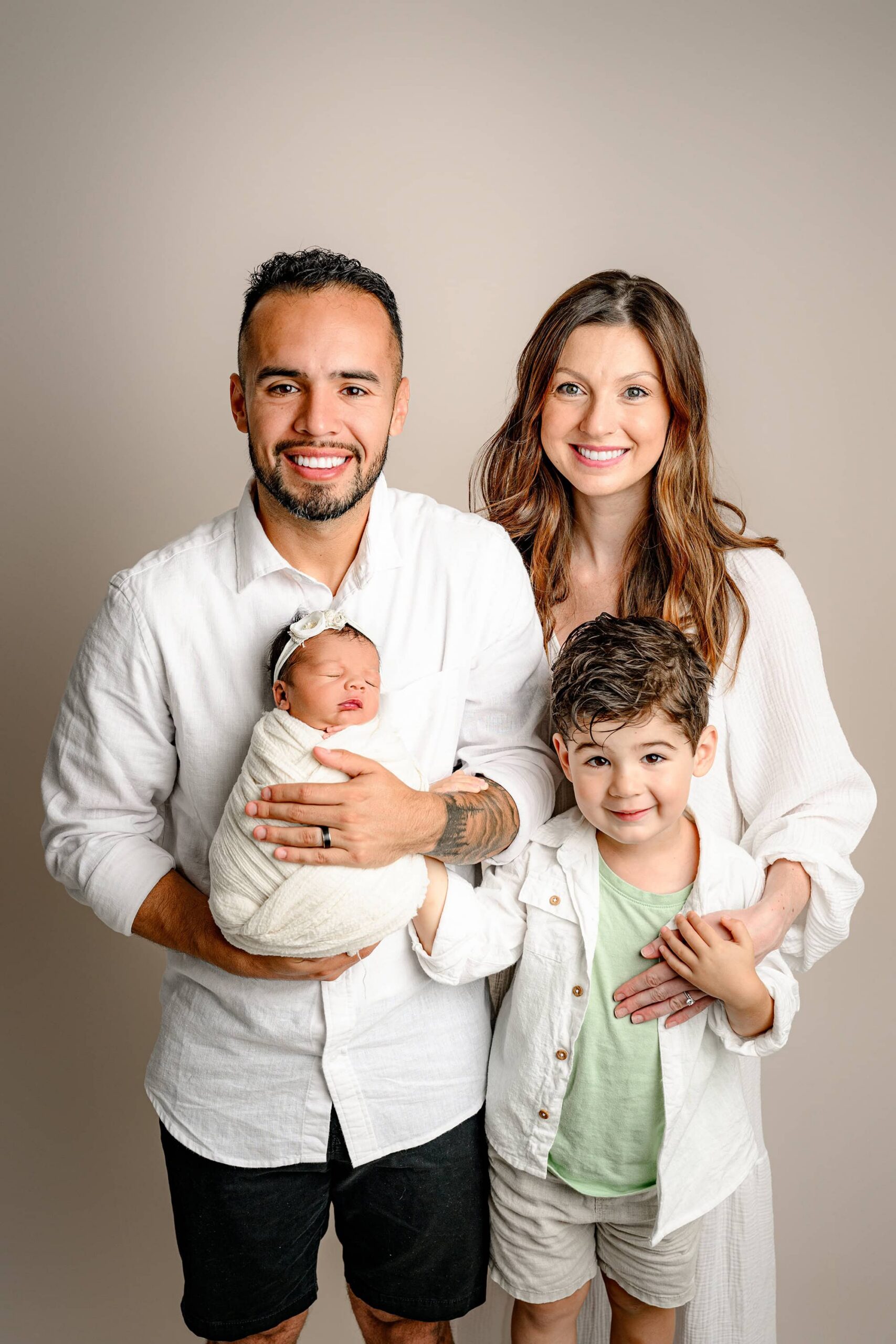 charlotte family of four dressed in white holding their newborn daughter during family photos